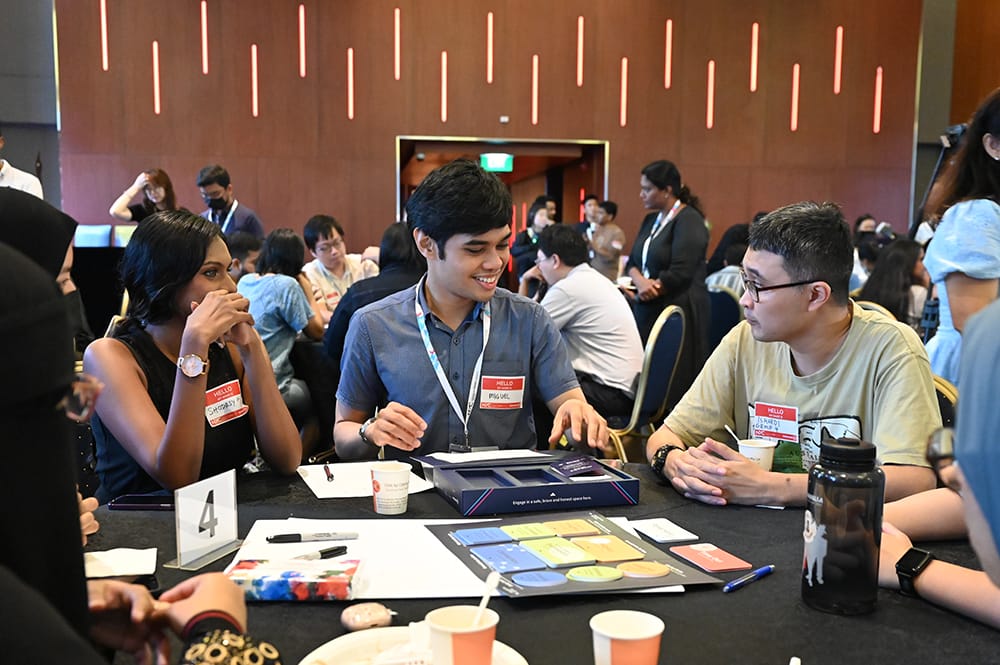 People at table playing card game, table number visible. Attendees wear name tags.