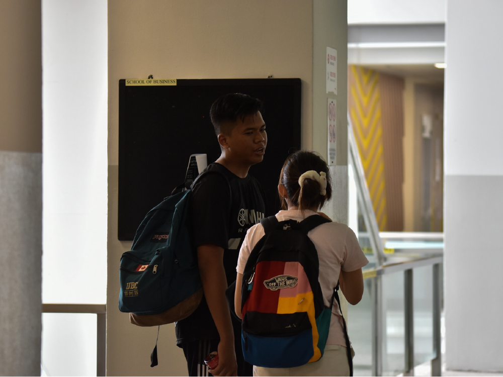 Two students with backpacks talking near a School of Business sign