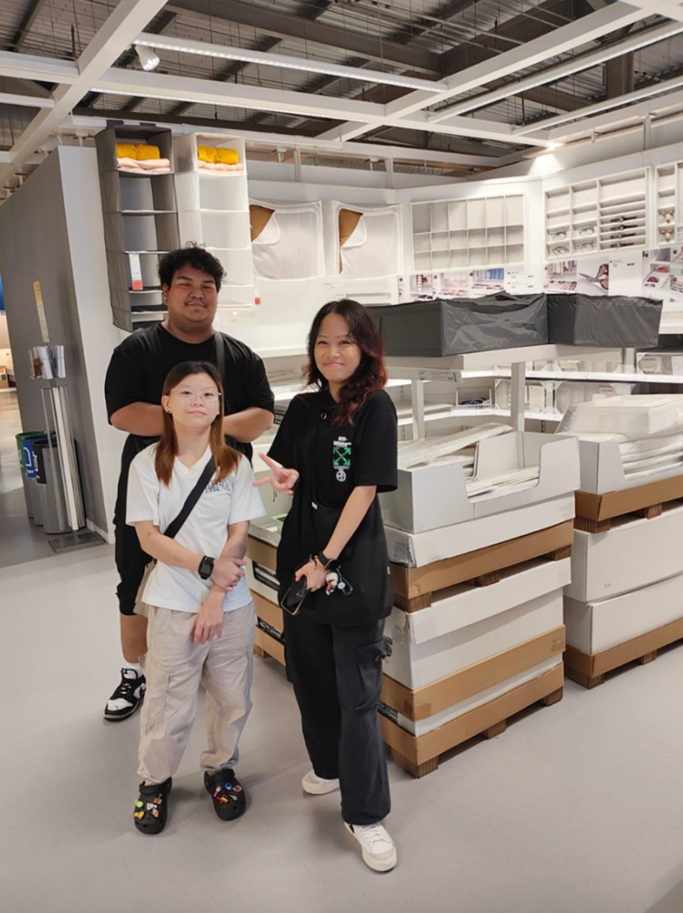 Three people stand in an IKEA store aisle with shelving, bins and boxed items.
