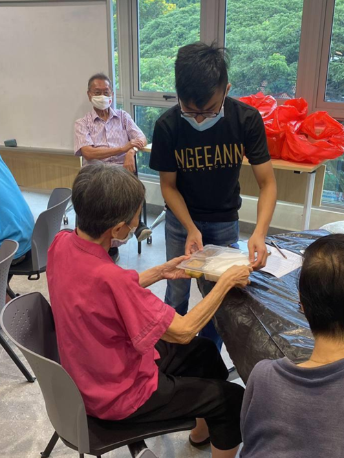 Toh Guan Ru handing a meal container to an elderly woman at a distribution event