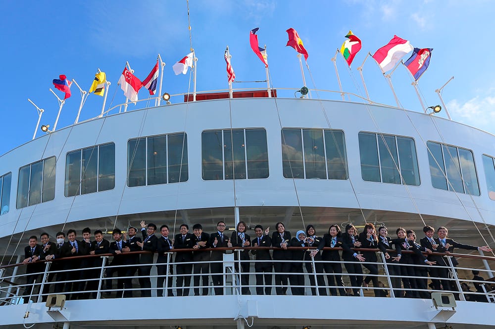 Group of people in suits on a cruise ship deck with international flags.