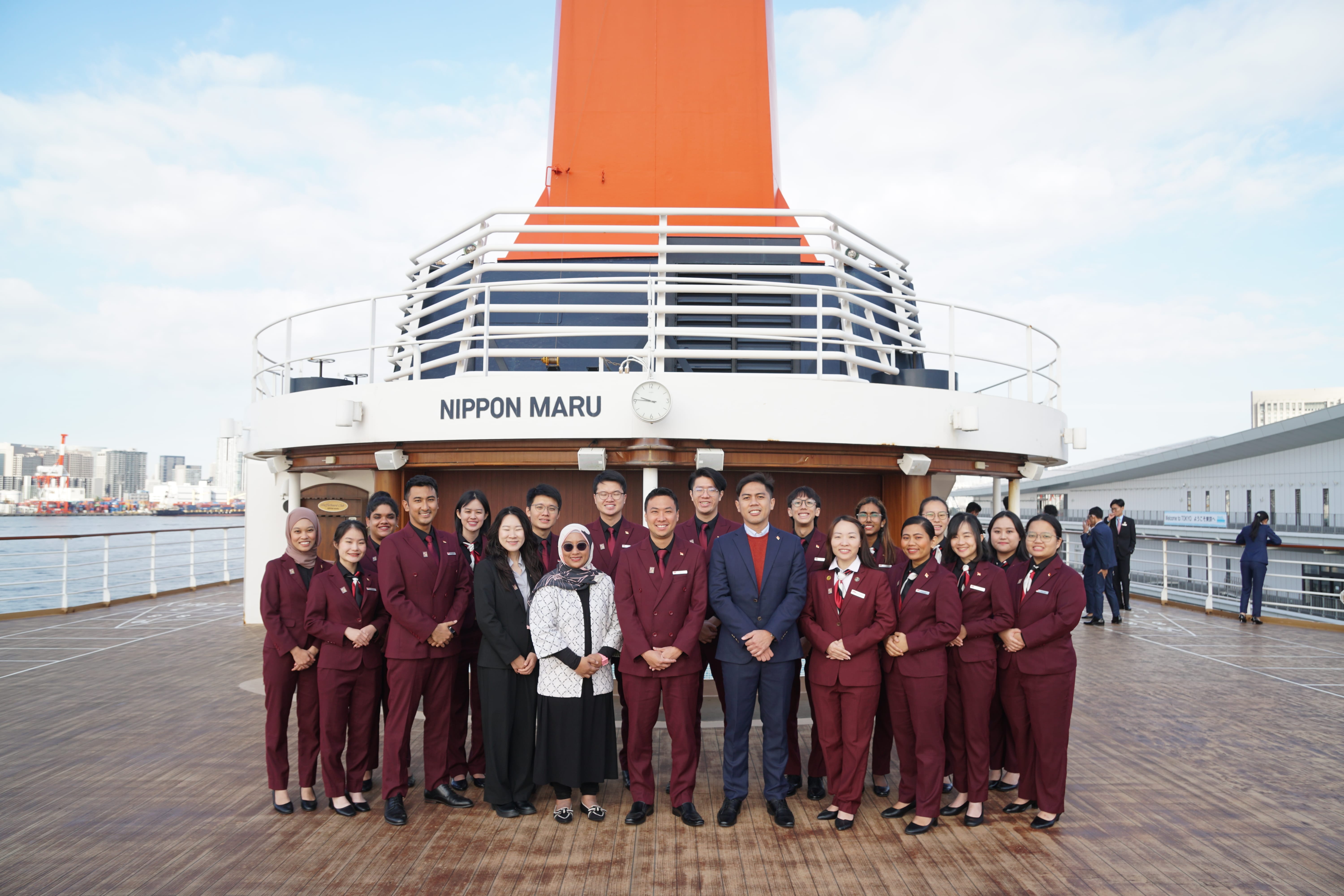 Group of people in red suits posing with guests on the cruise ship deck.