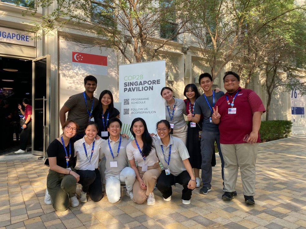 Group of people standing near COP28 Singapore Pavilion sign with Singapore flag.