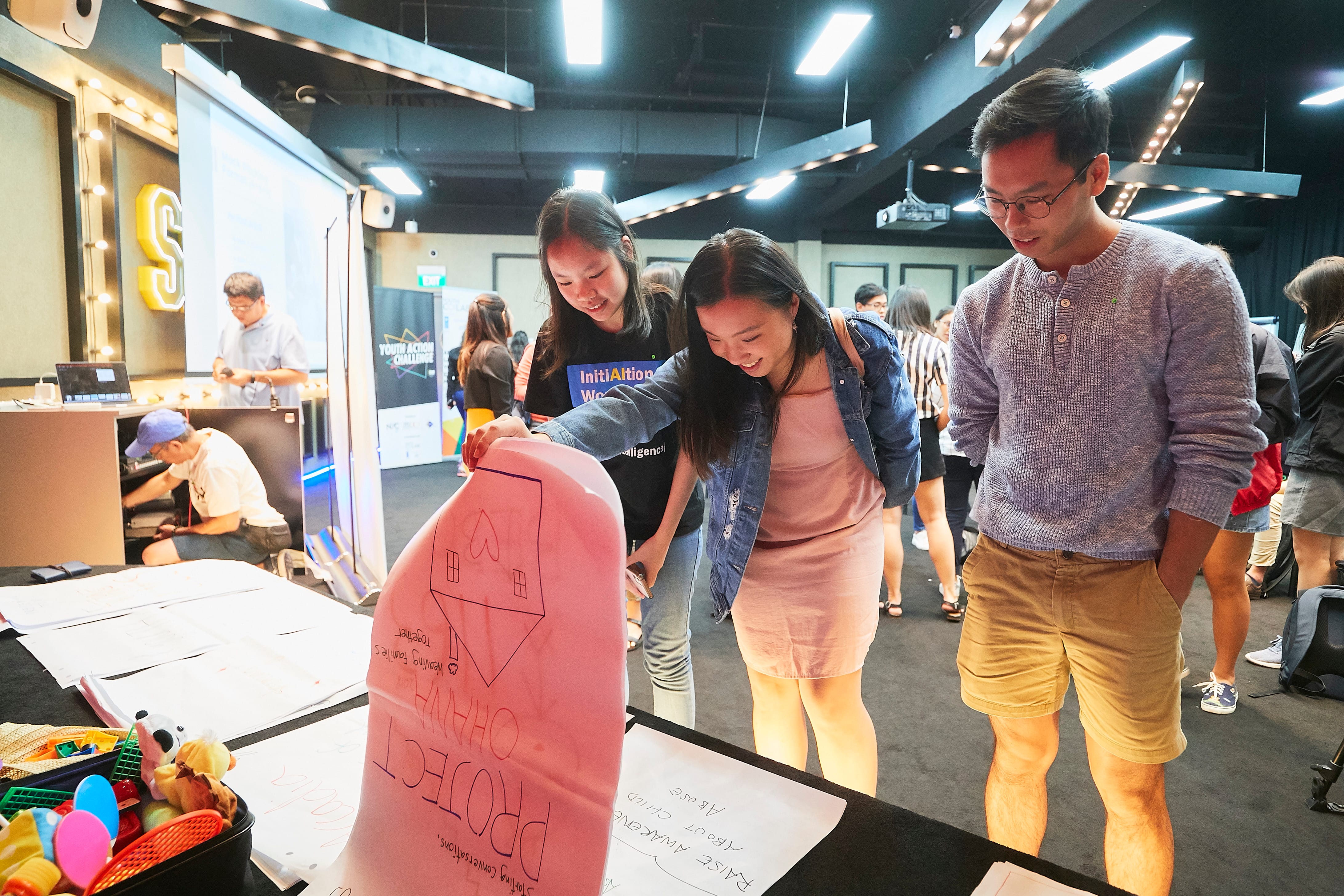 Attendees review youth project ideas displayed on posters at an indoor event.