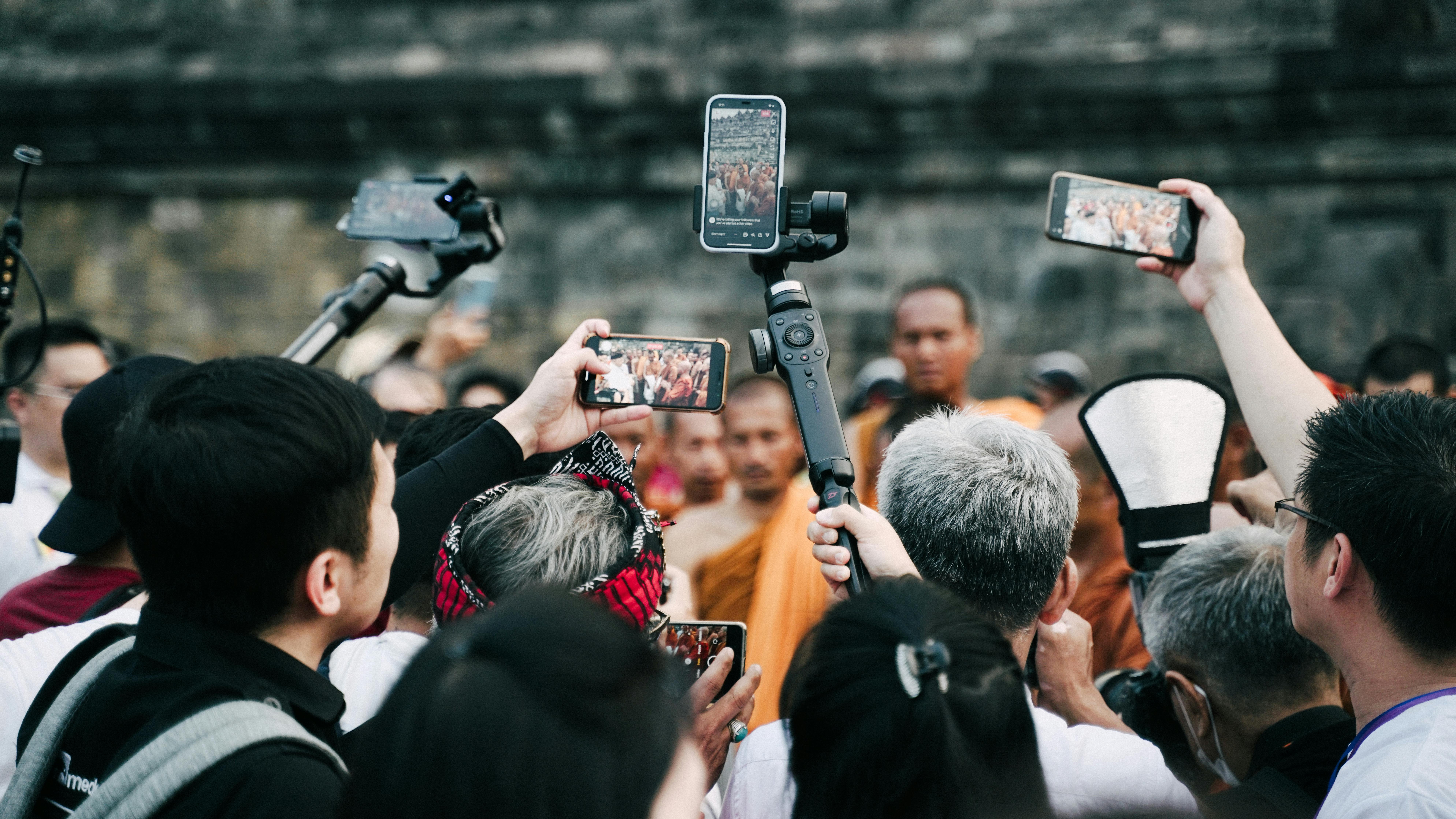 Crowd holds up phones to record monks. Phones display video of the same scene.
