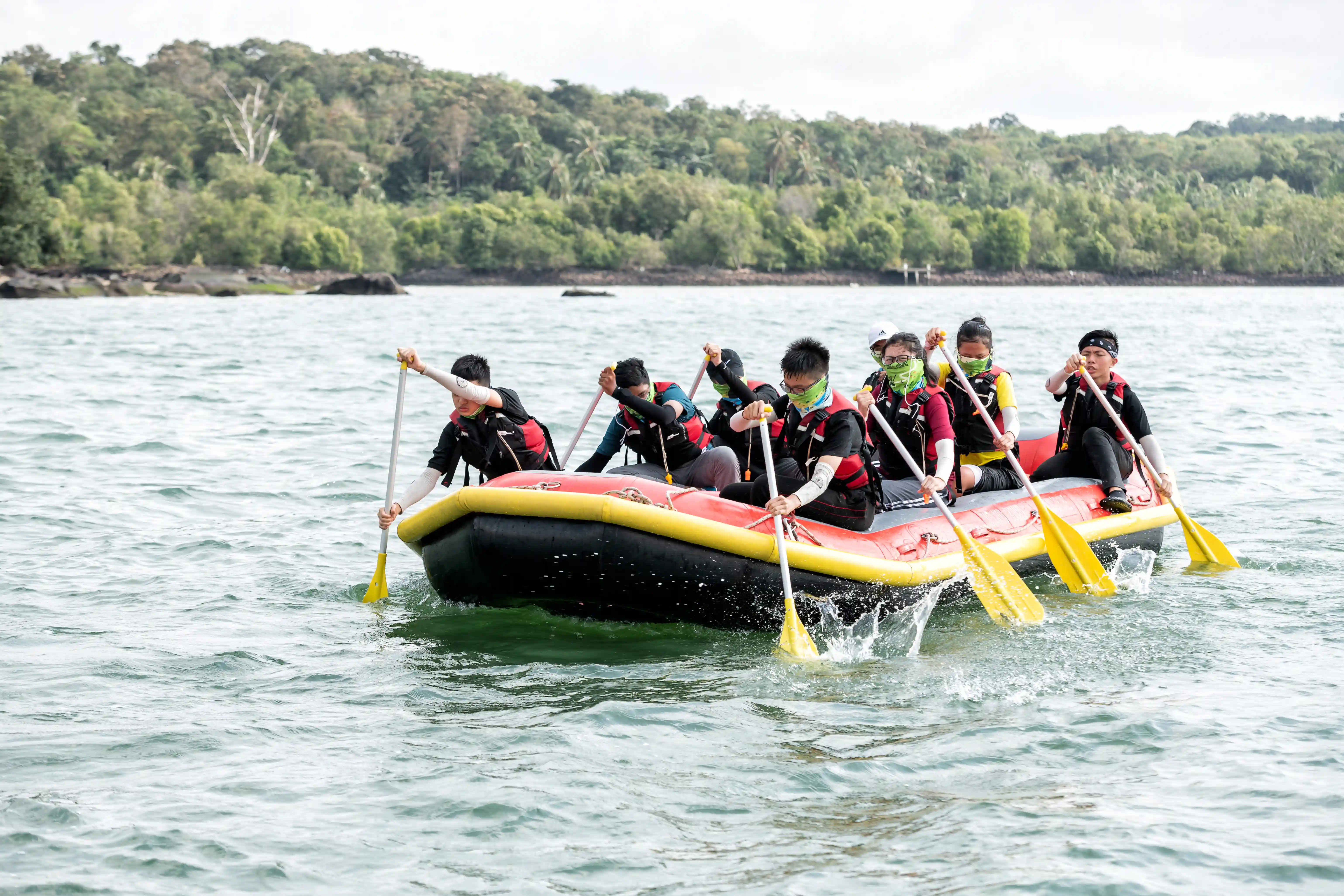 Group of participants in life vests paddling in a raft during a team-building water activity.