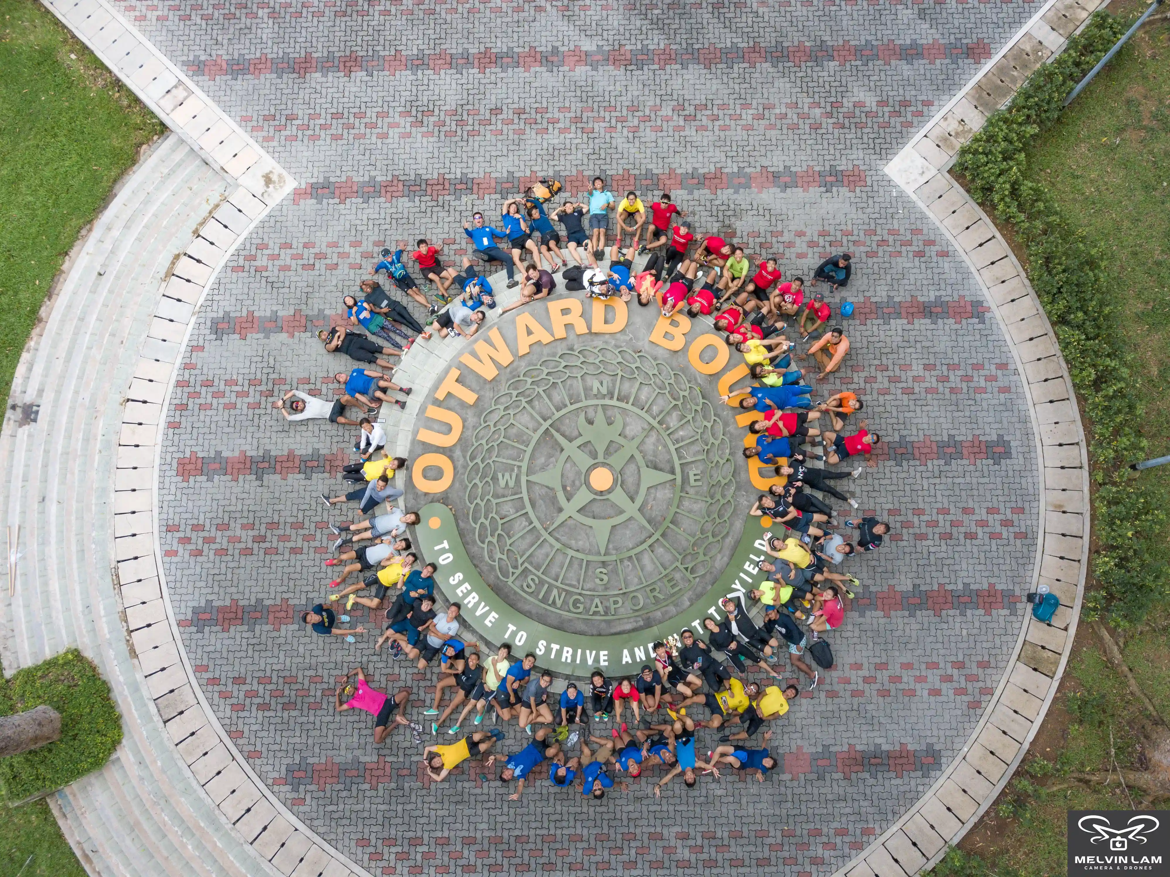 Aerial view of OBS participants forming circle around compass logo on paved plaza at Pulau Ubin campus.