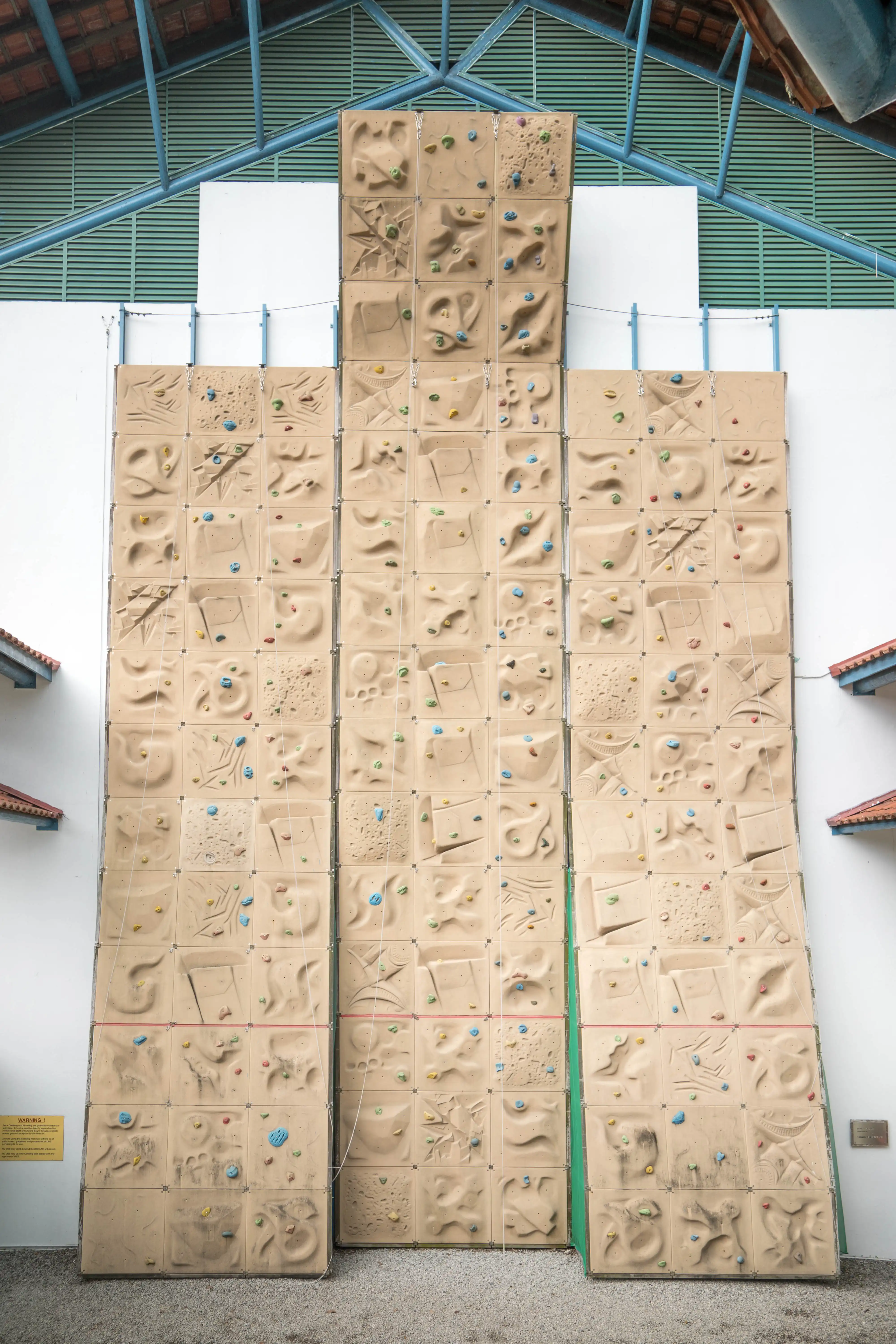 Large indoor rock climbing wall with colorful holds arranged in modular panels under metal roof.