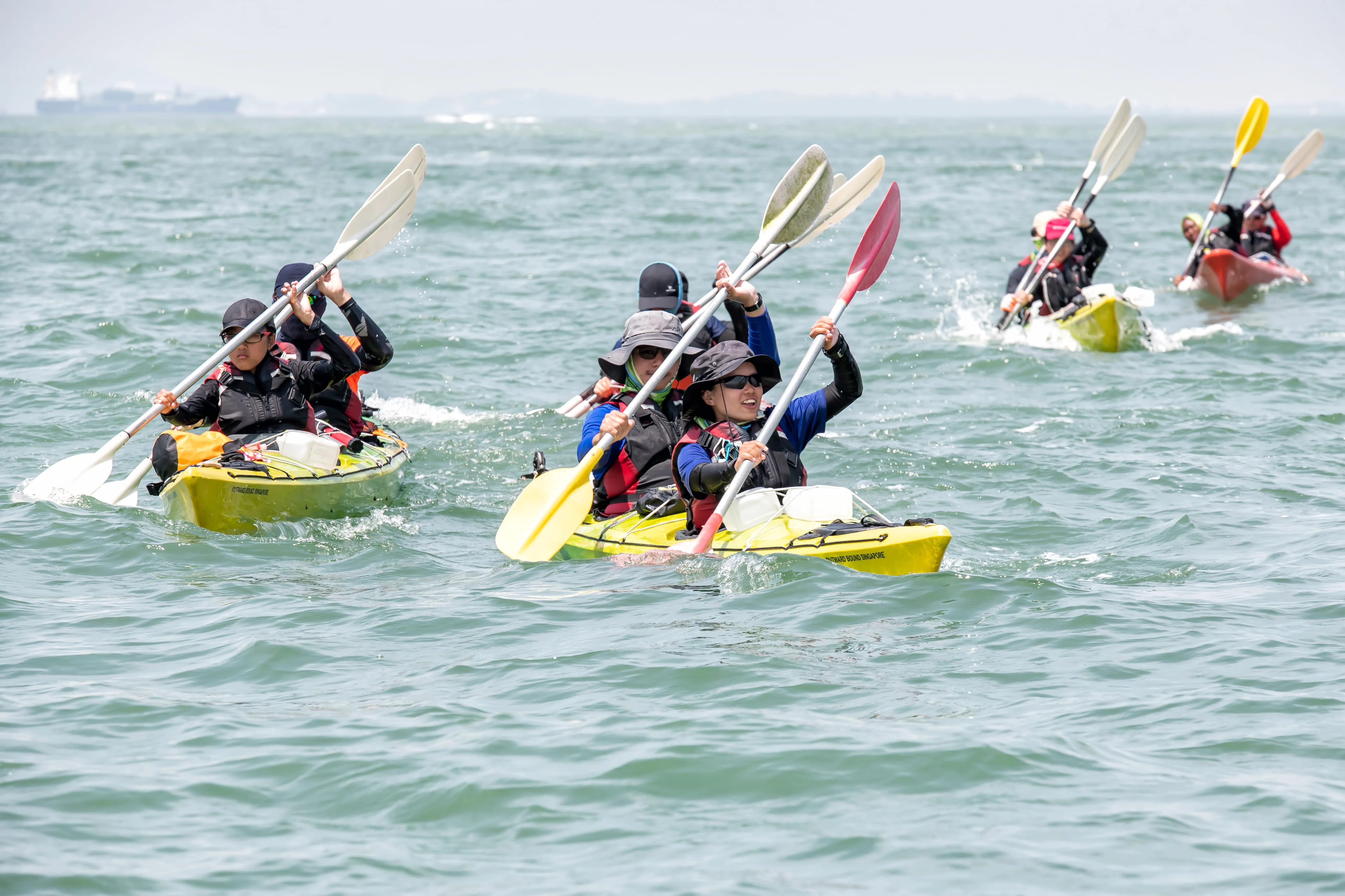 Groups of people in life vests and hats kayaking in open water.