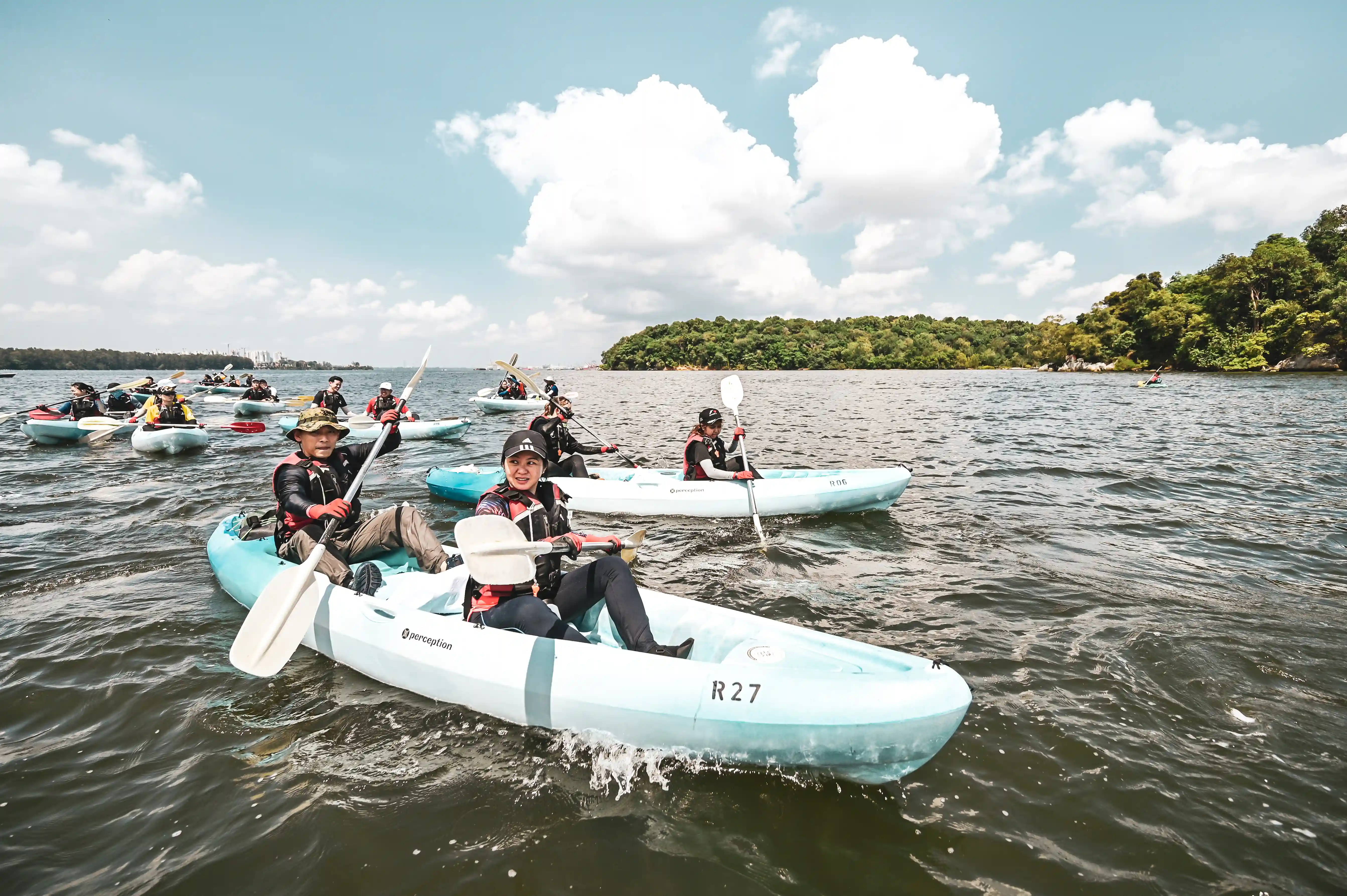Groups of OBS kayakers paddle together in open water under bright skies and sun.