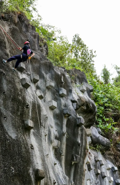 Person in helmet rock climbing on gray stone wall with ropes.
