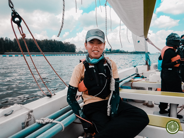 Smiling participant seated on a sailing boat during OBS expedition on calm waters.