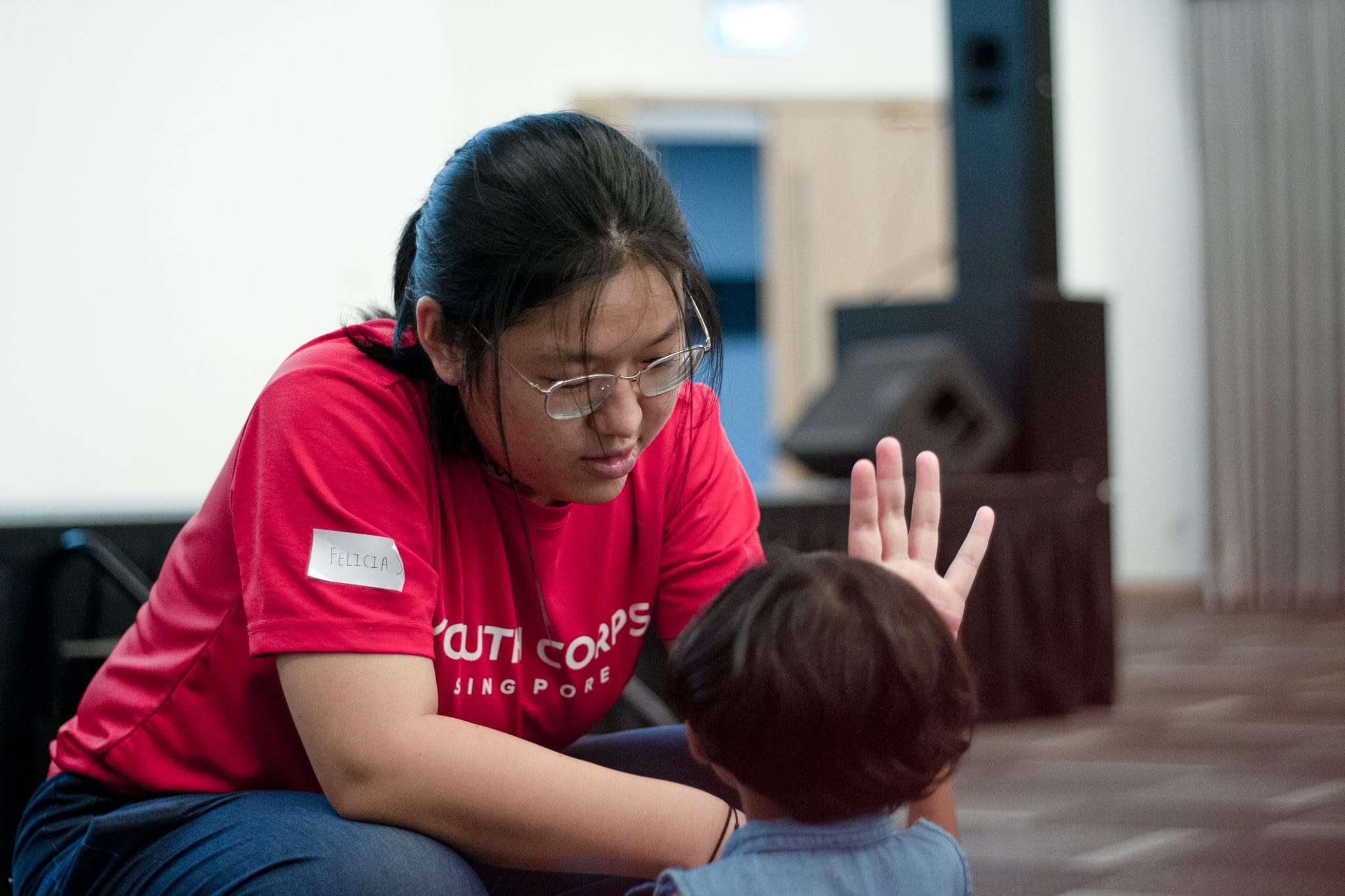 Girl in red Youth Corps shirt high-fives a child.