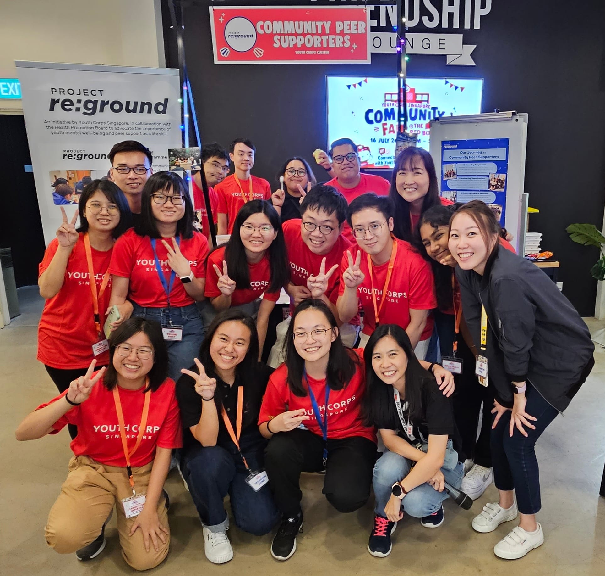 A group of Youth Corps volunteers posing together in front of the Project re:ground Community Peer Supporters booth at the Community Fair 2023.