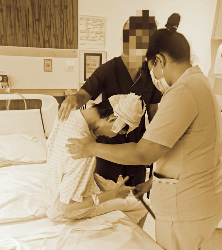 Jessica after surgery seated on a hospital bed and assisted by 2 nurses