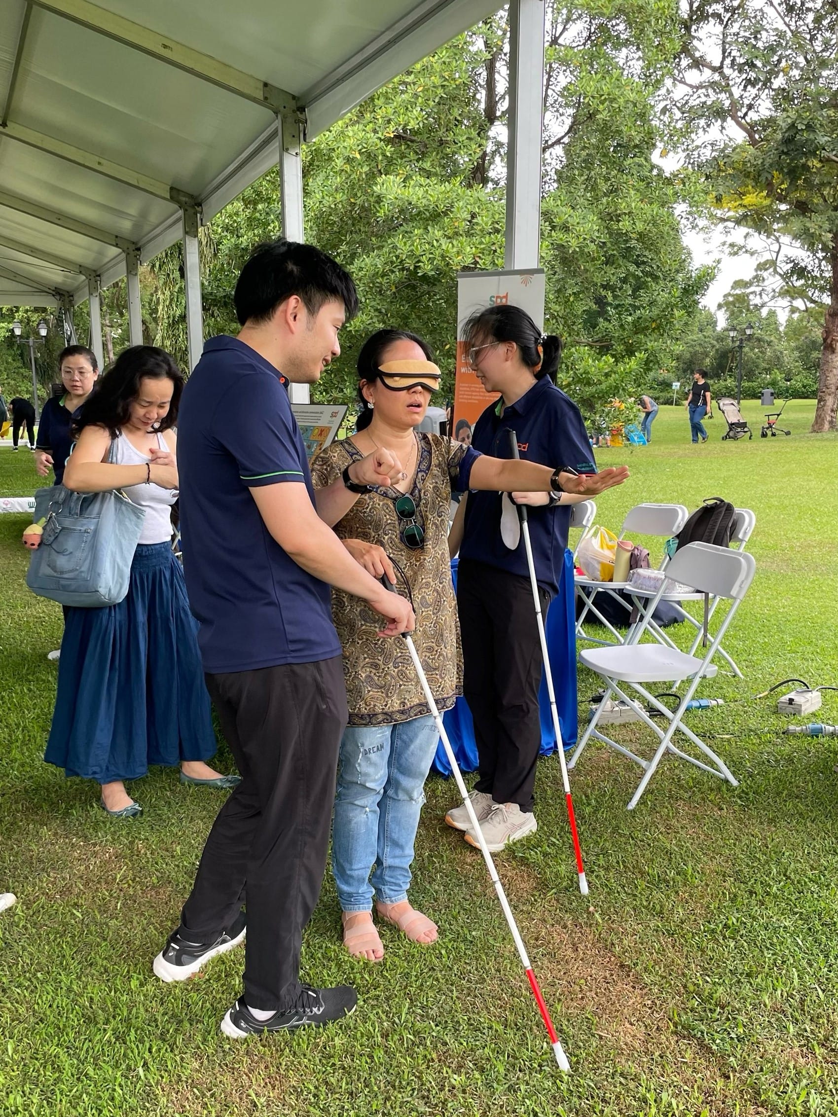 Woman blindfolded holding walking stick, guided by staff from SPD