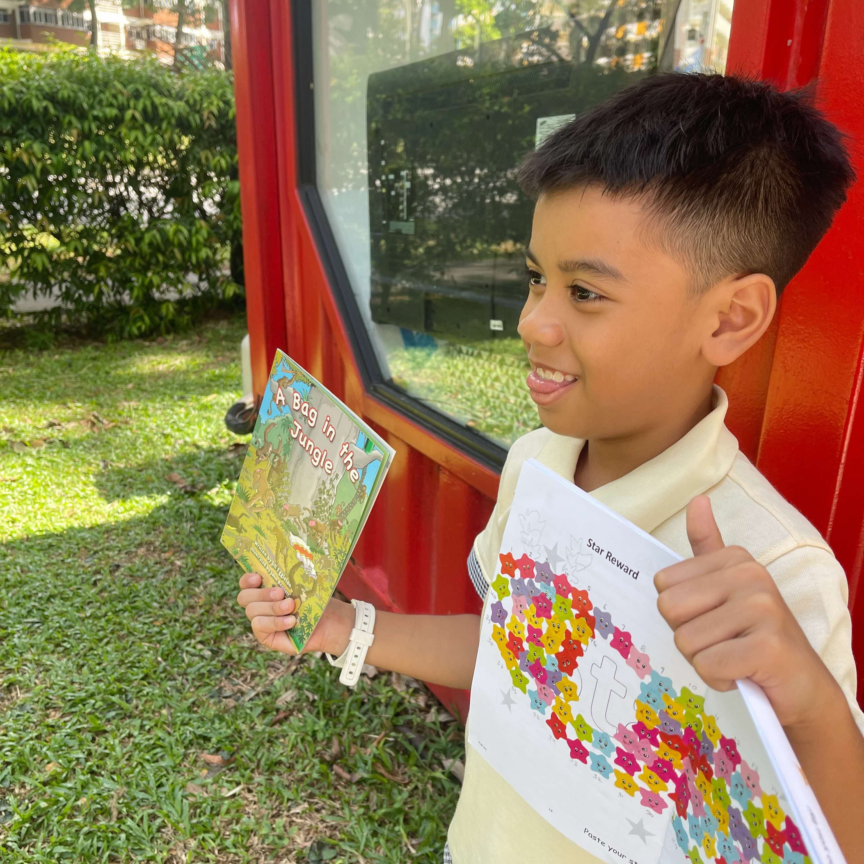 Boy holding up a workbook smiling.