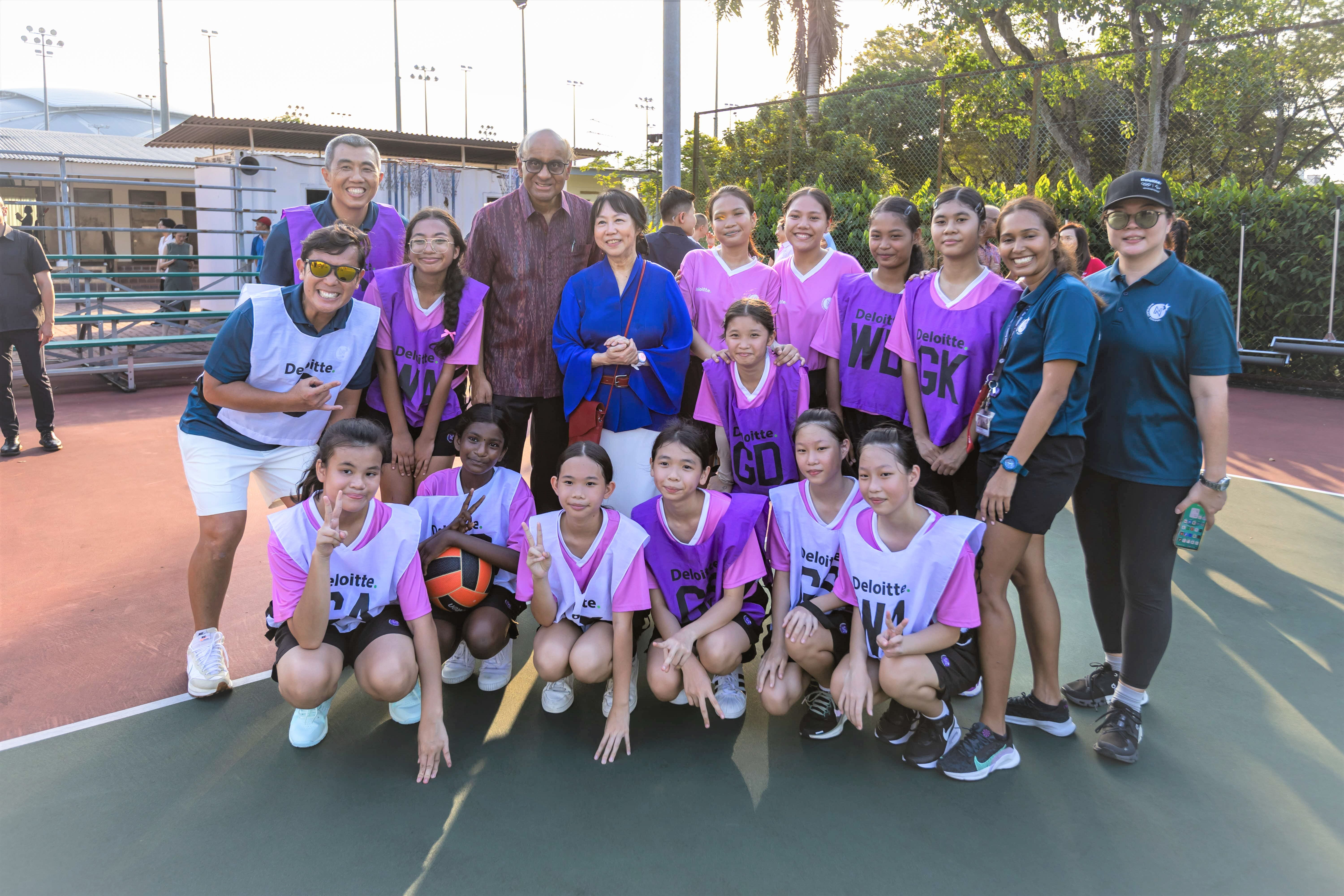 Group photo of President Tharman with netball players and coaches on court.