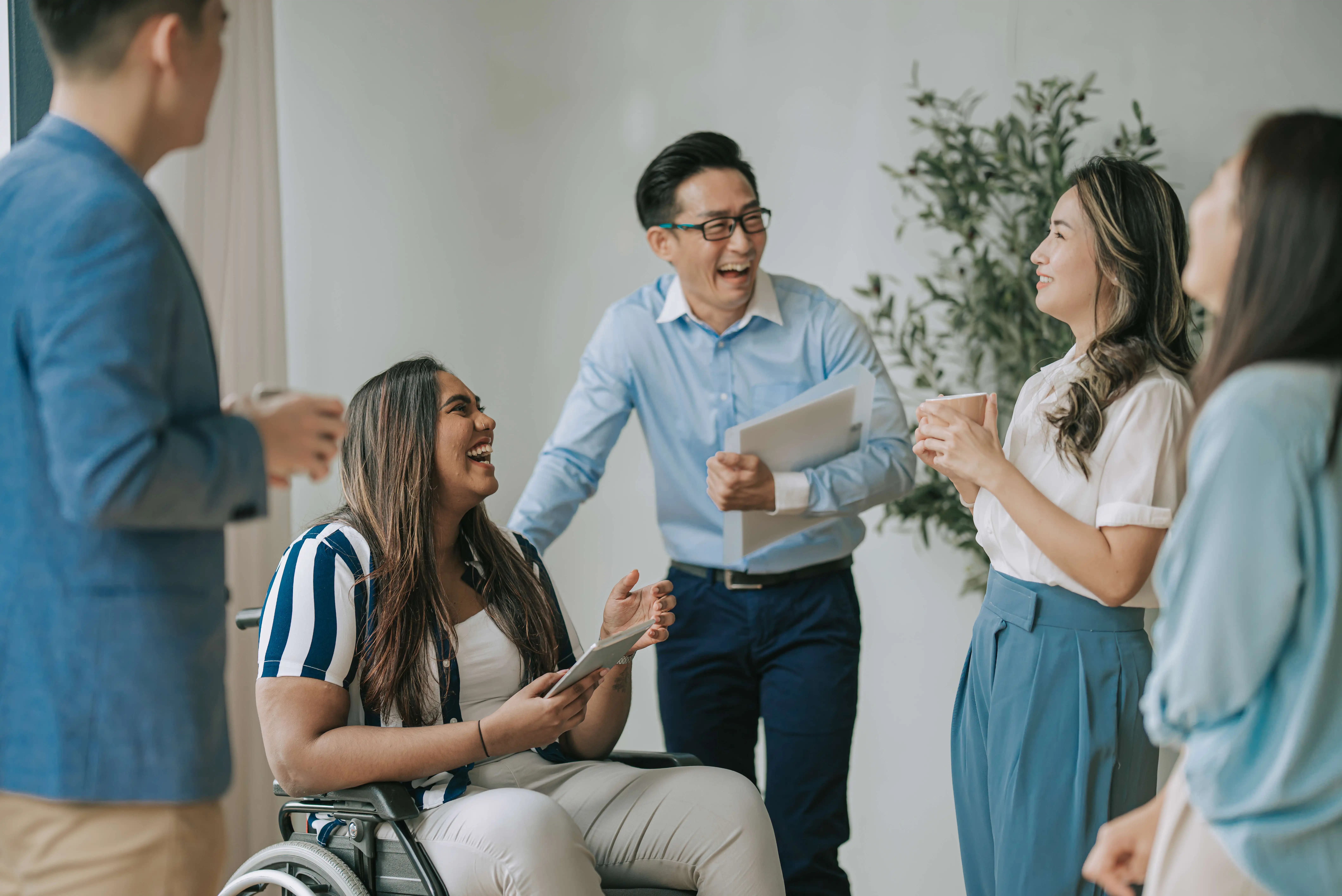 Group of colleagues, including a woman in a wheelchair, laughing and talking together indoors