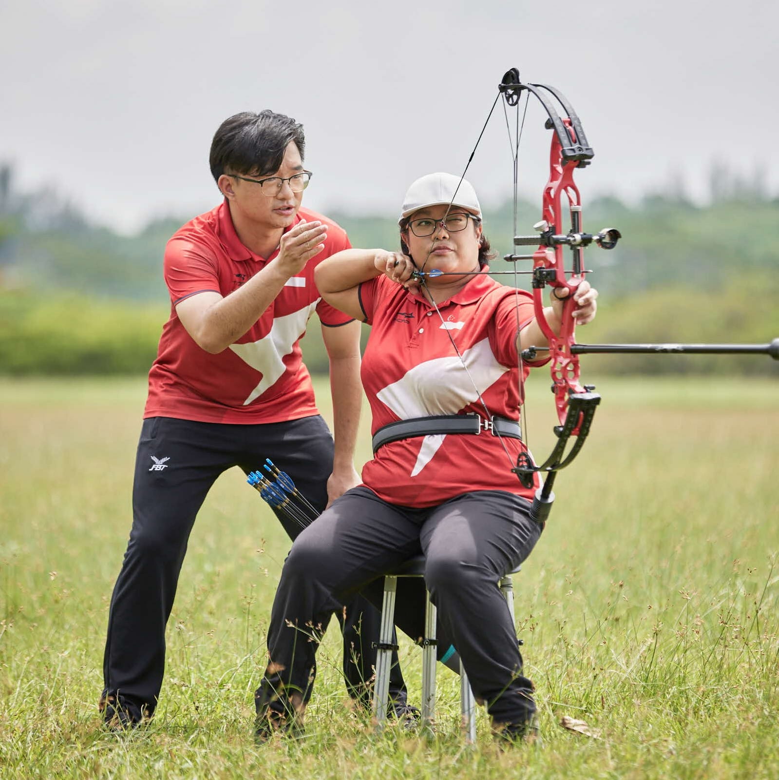 Archery instructor guiding Nur Syahidah Alim on form during an outdoor archery session.