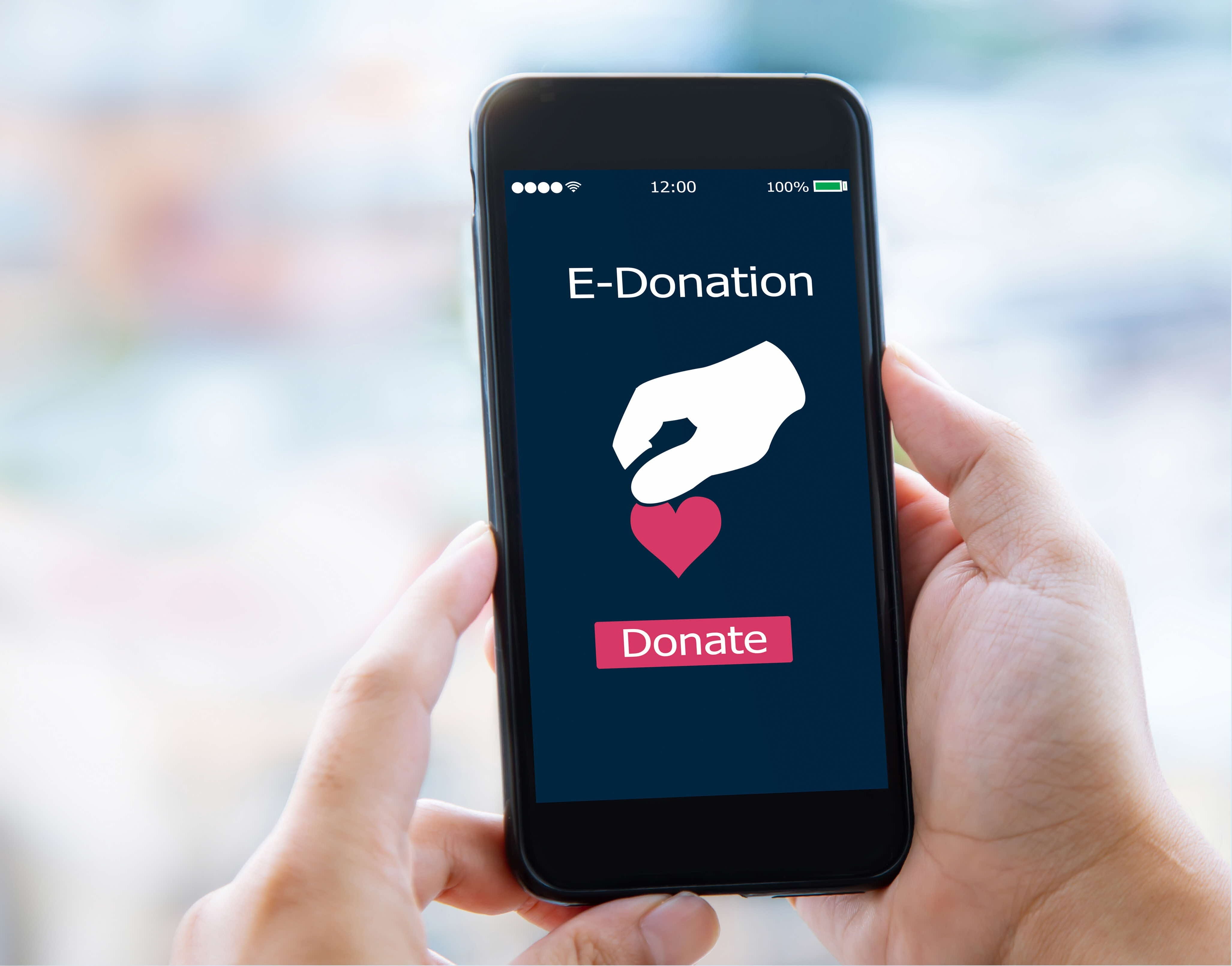 Hands holding smartphone displaying 'E-Donation' app with heart icon and red 'Donate' button