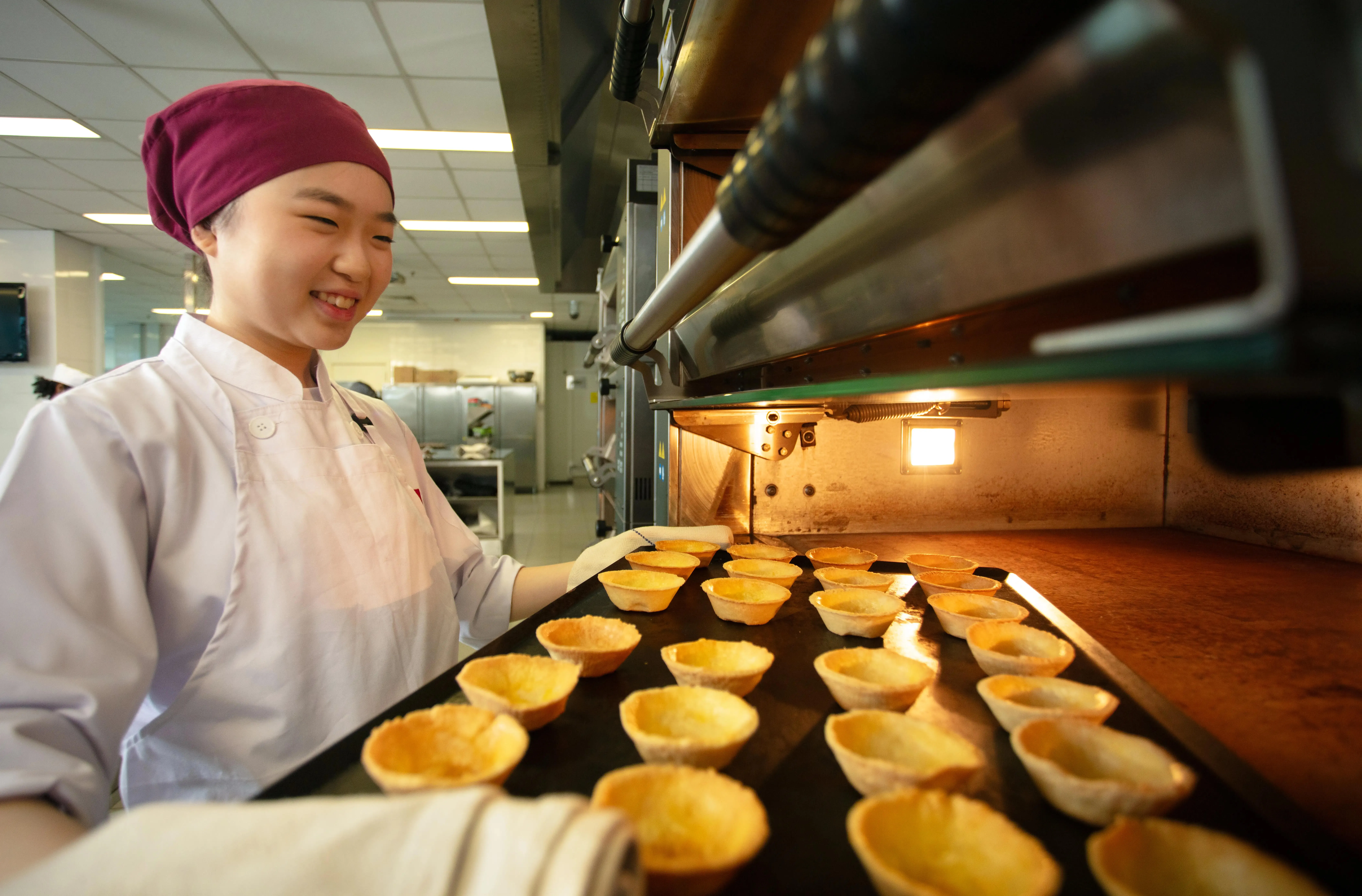 Baker wearing whites removes tray of tart shells from a commercial oven.