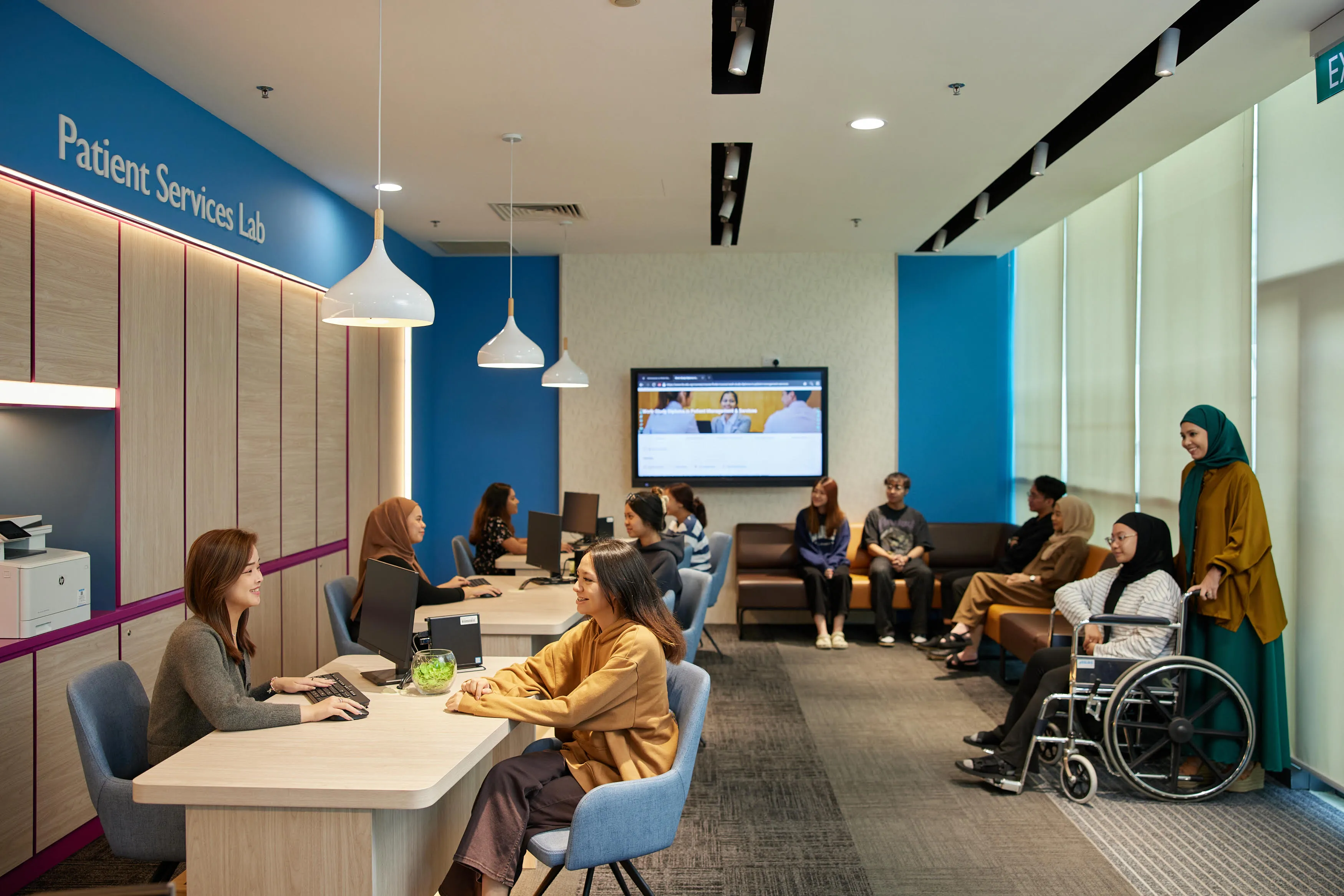 Patient services lab with people at desks, waiting on couches, and one in a wheelchair.
