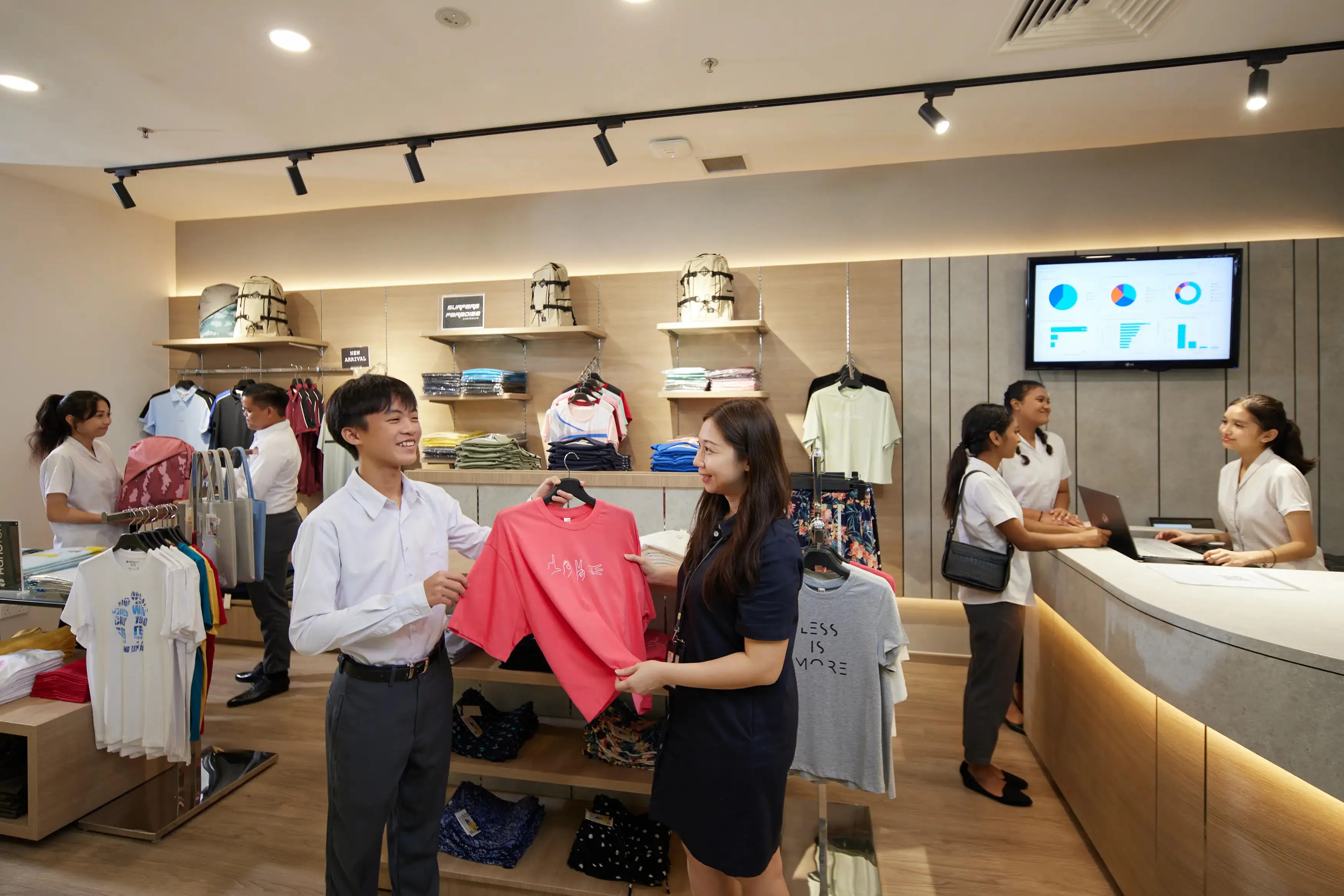 Retail store interior with staff assisting a customer with a pink t-shirt.