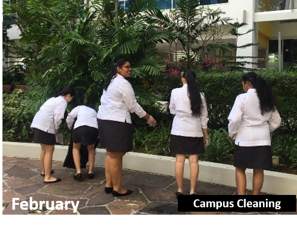 Four people in white shirts and black skirts picking up trash outside near green plants.