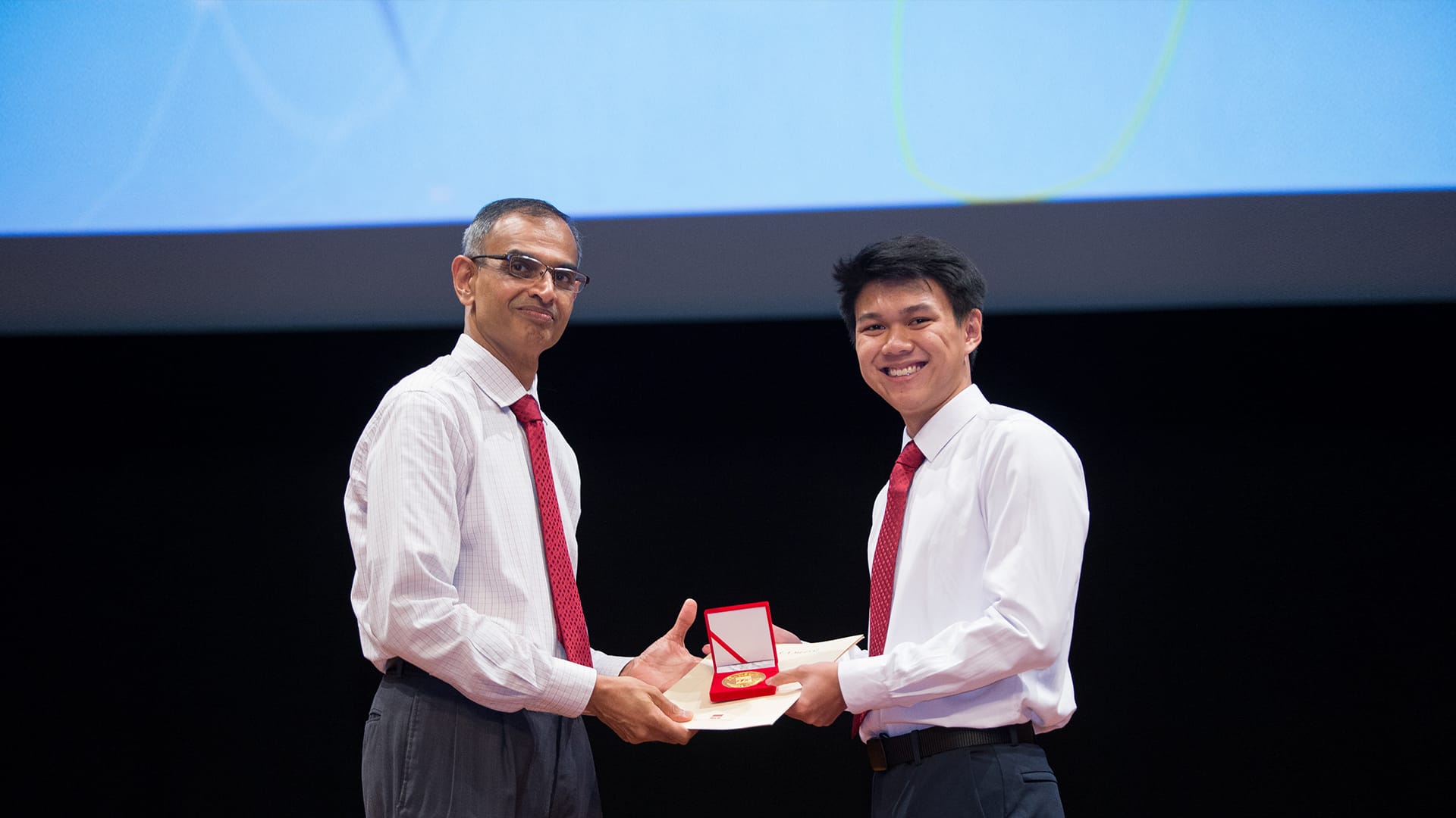 Man presents a student with a medal and certificate on stage.