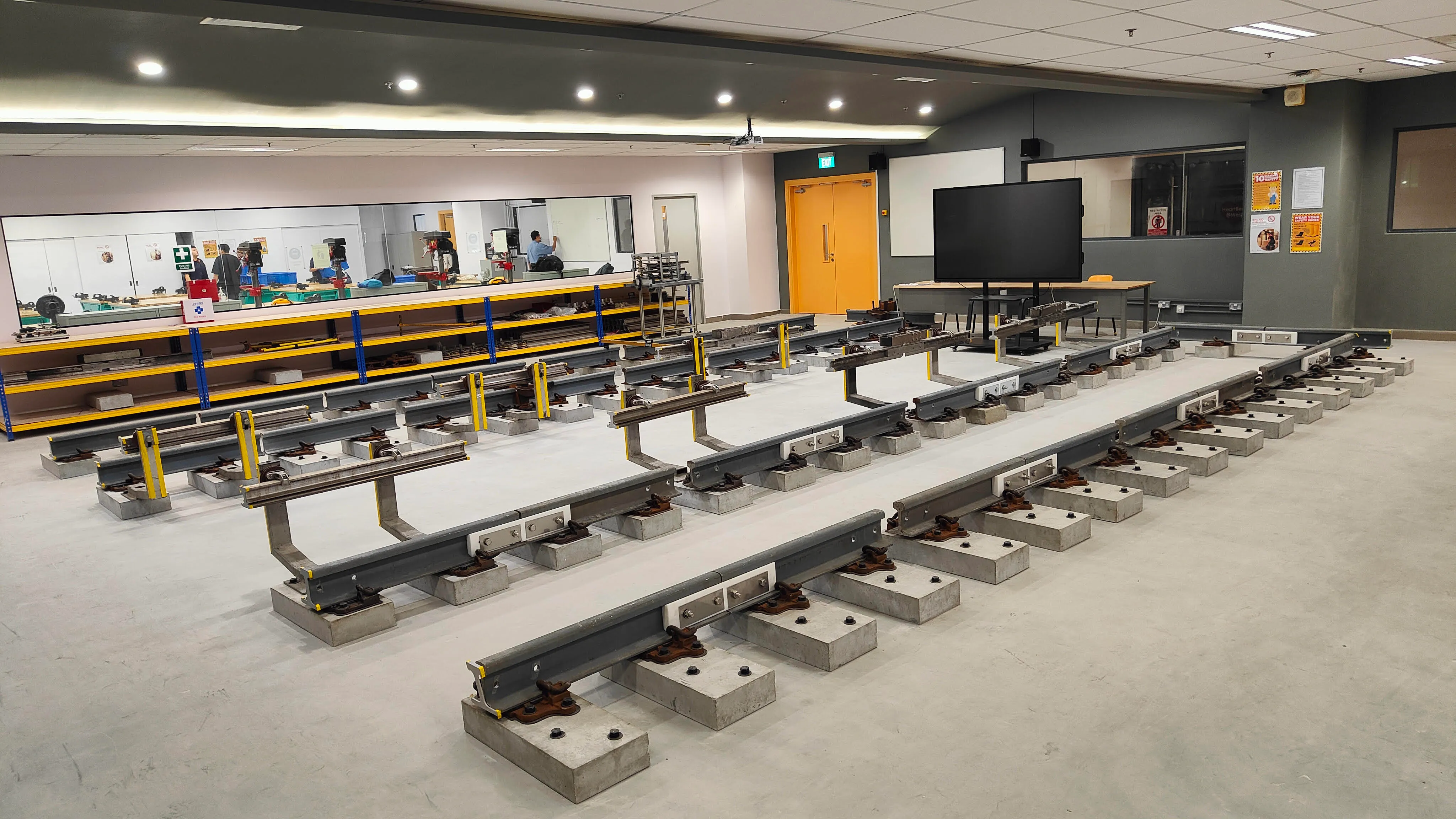 Classroom with multiple sections of rail track on concrete supports. Mirror, tables, and monitors visible.
