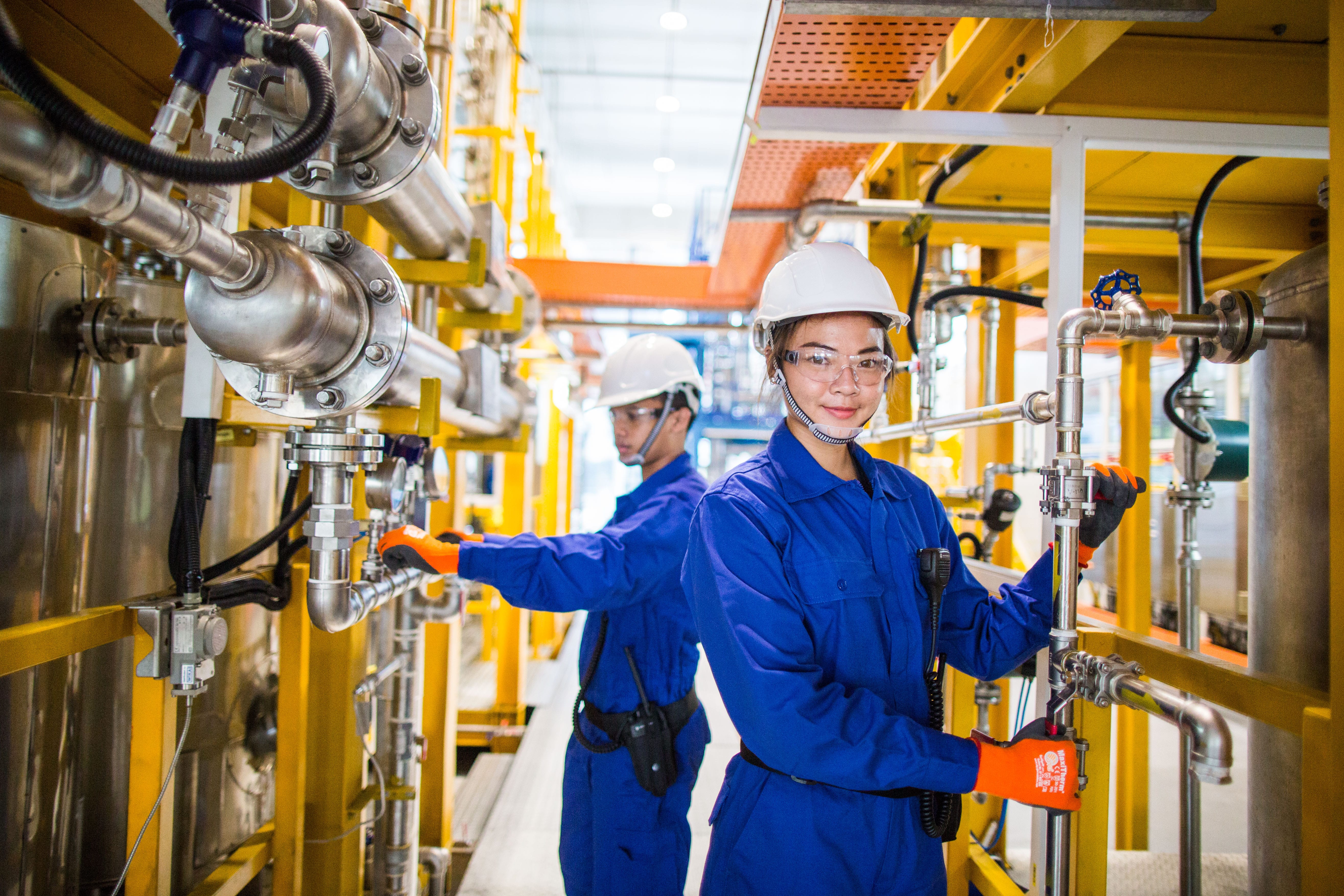 Two workers in blue containalls and helmets operating valves in an industrial training facility