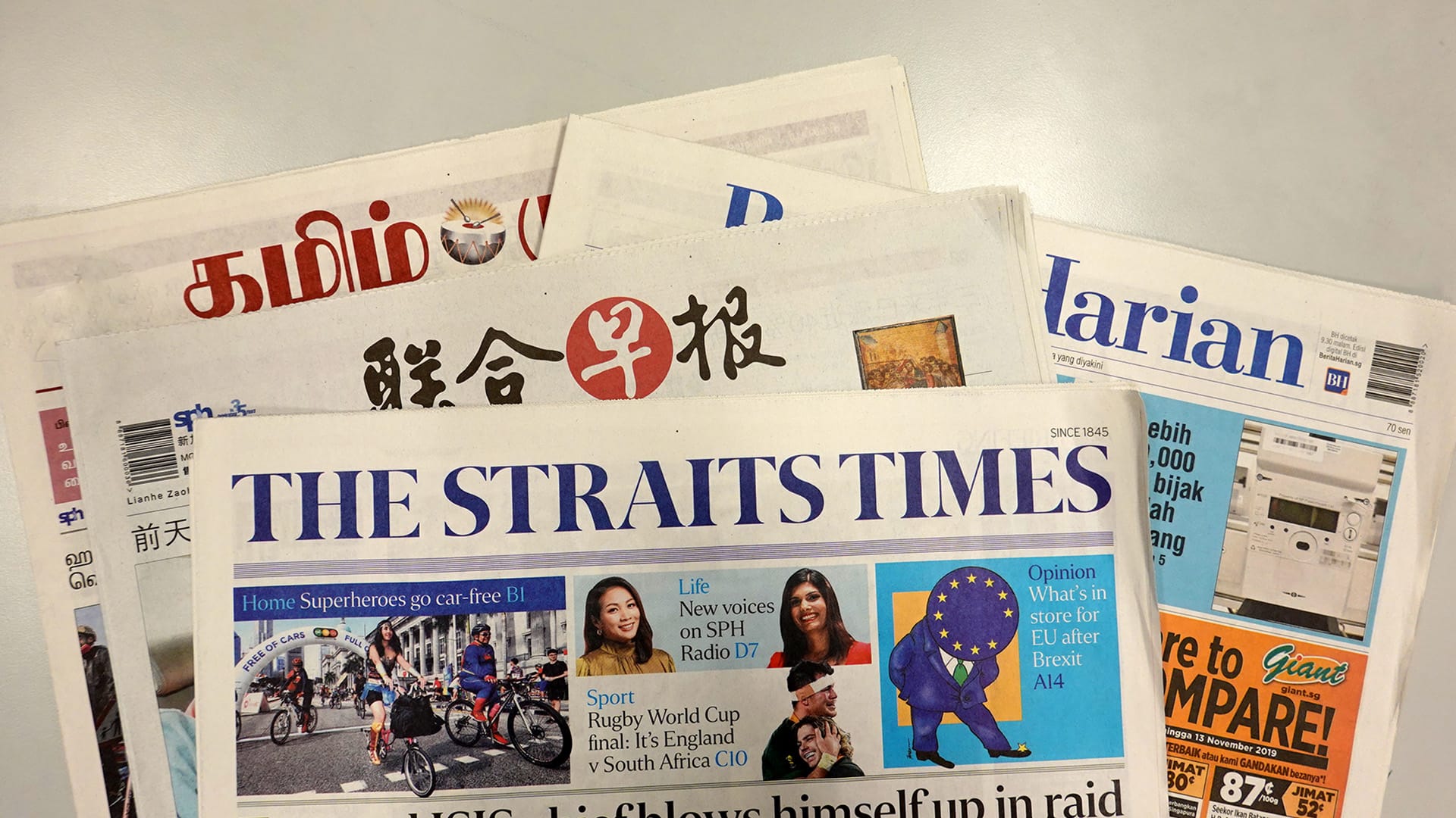 Stack of newspapers including The Straits Times, Lianhe Zaobao, Berita Harian, and Tamil Murasu.
