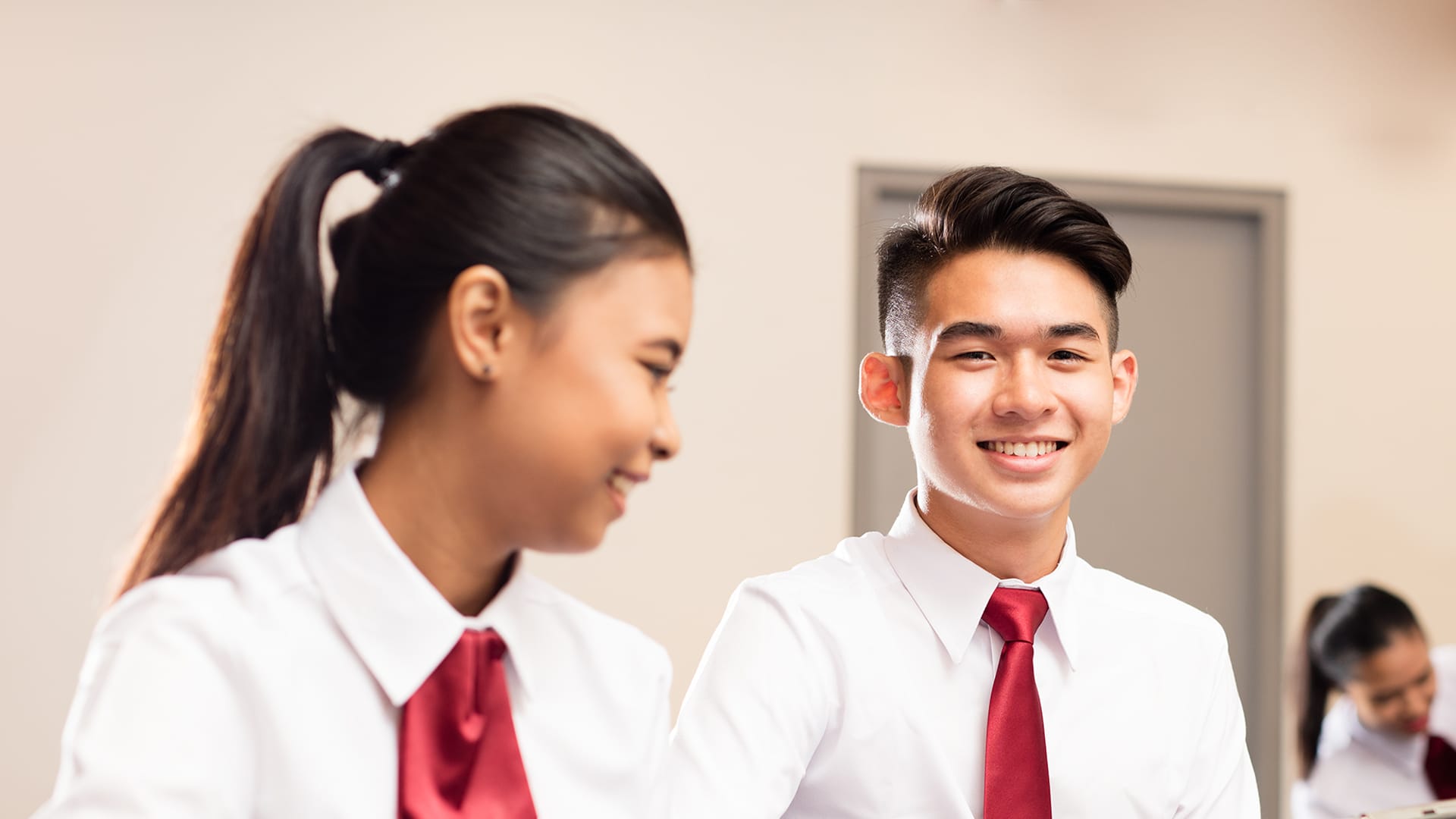 Two students in white shirts and red ties, one smiling at the viewer.