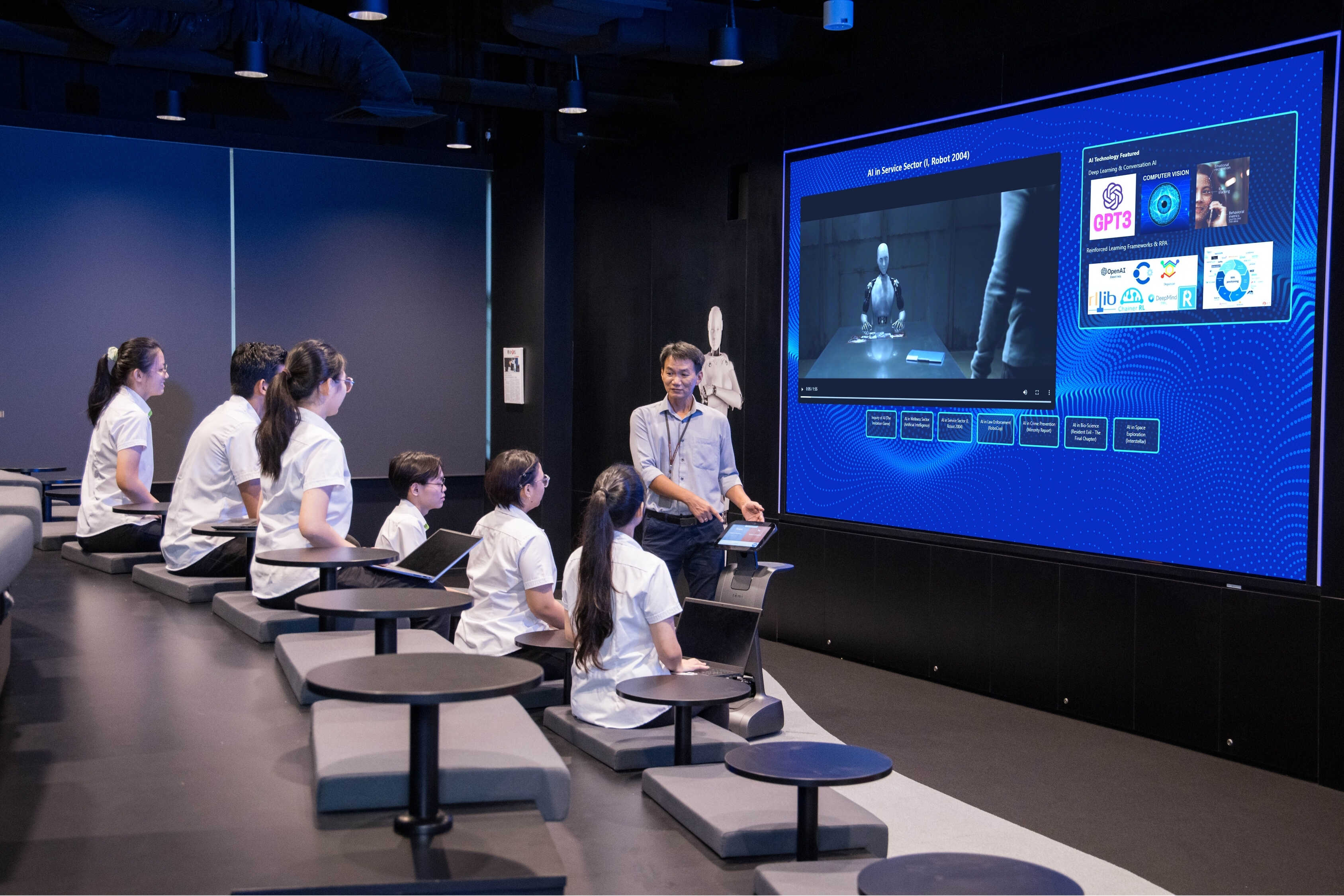 Students watch a presentation about AI, GPT3, and robotics on a large screen.