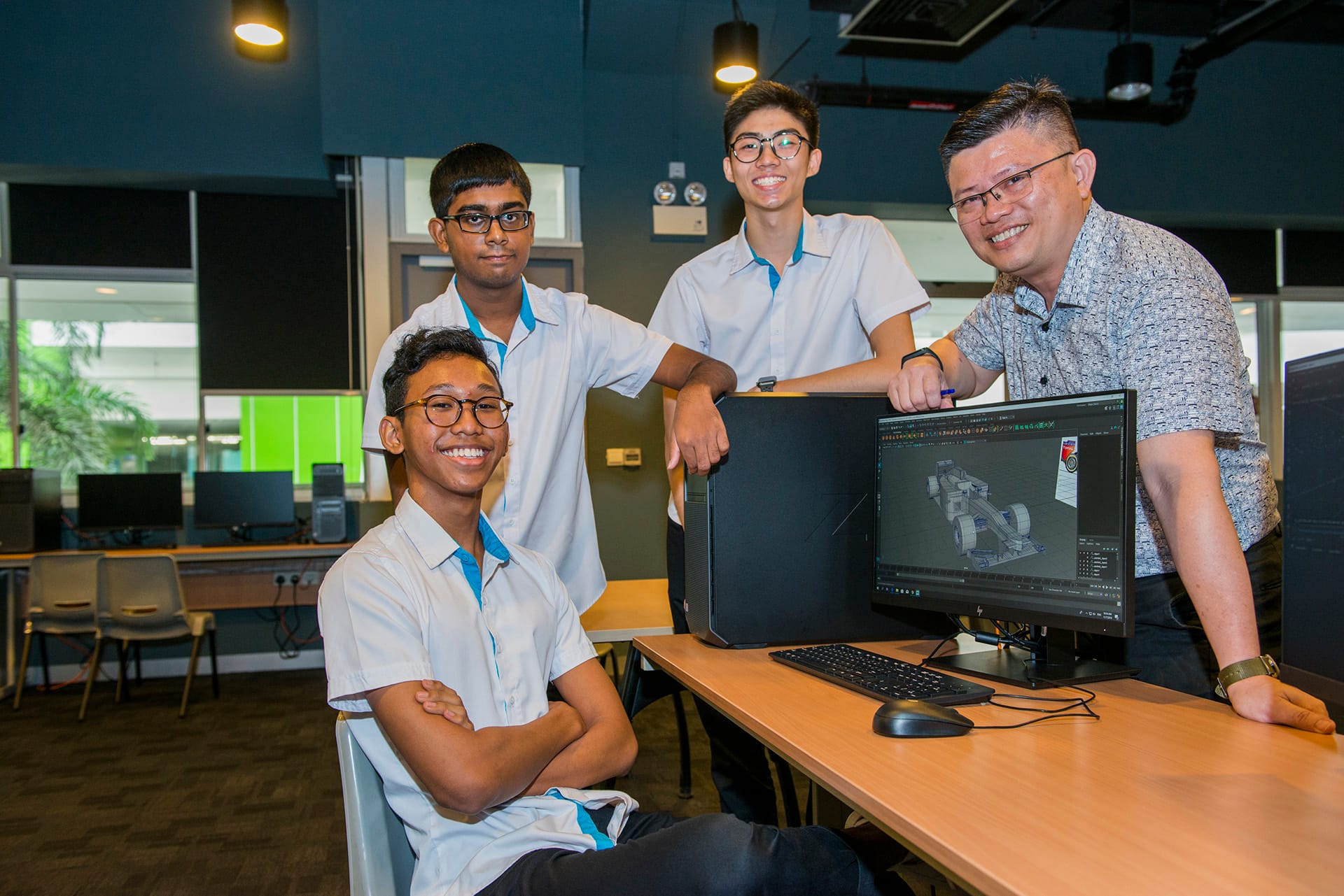 Students and instructor posing in computer lab with 3D model of race car on screen