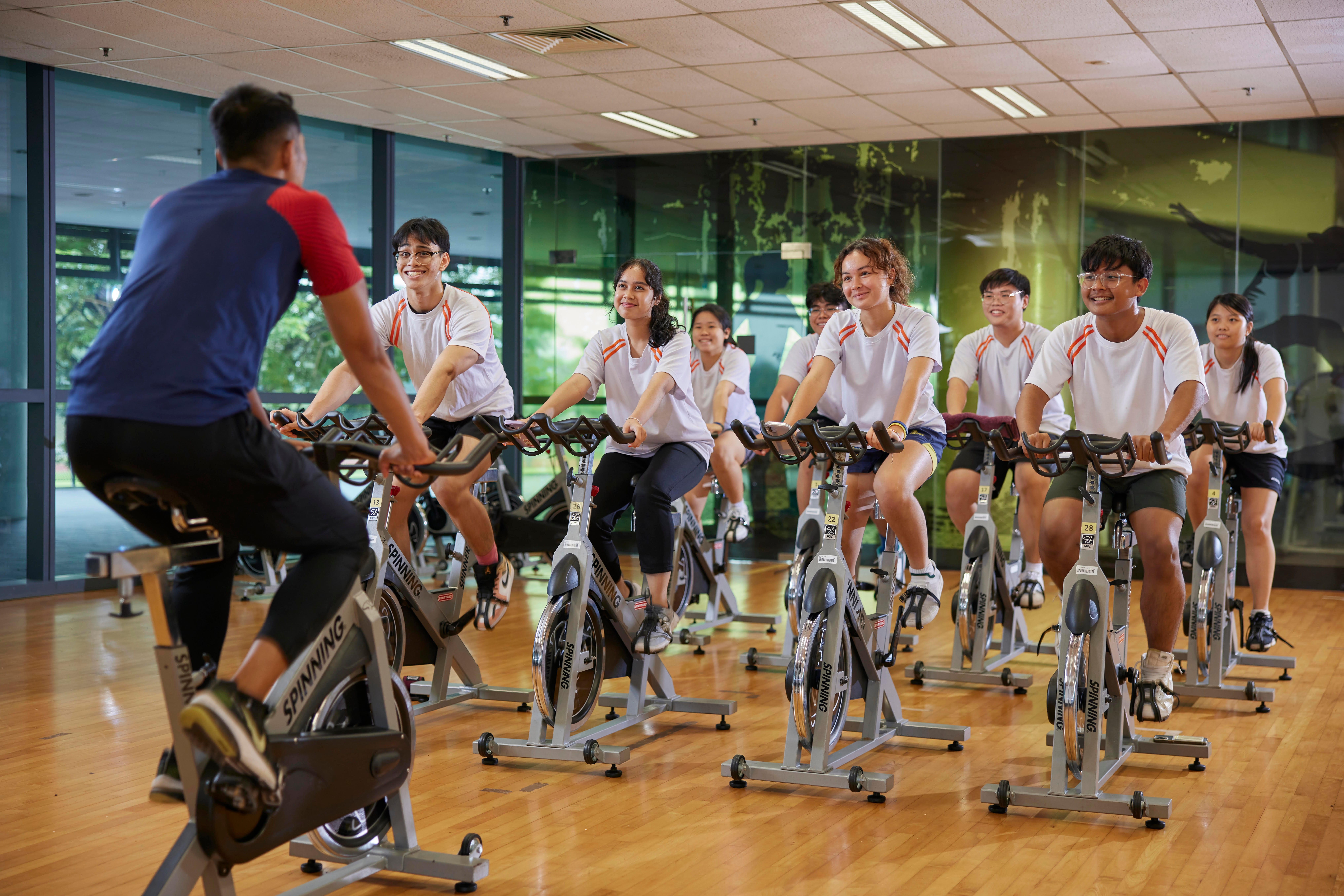 Group cycling class; students on /'Spinning/' bikes with instructor.