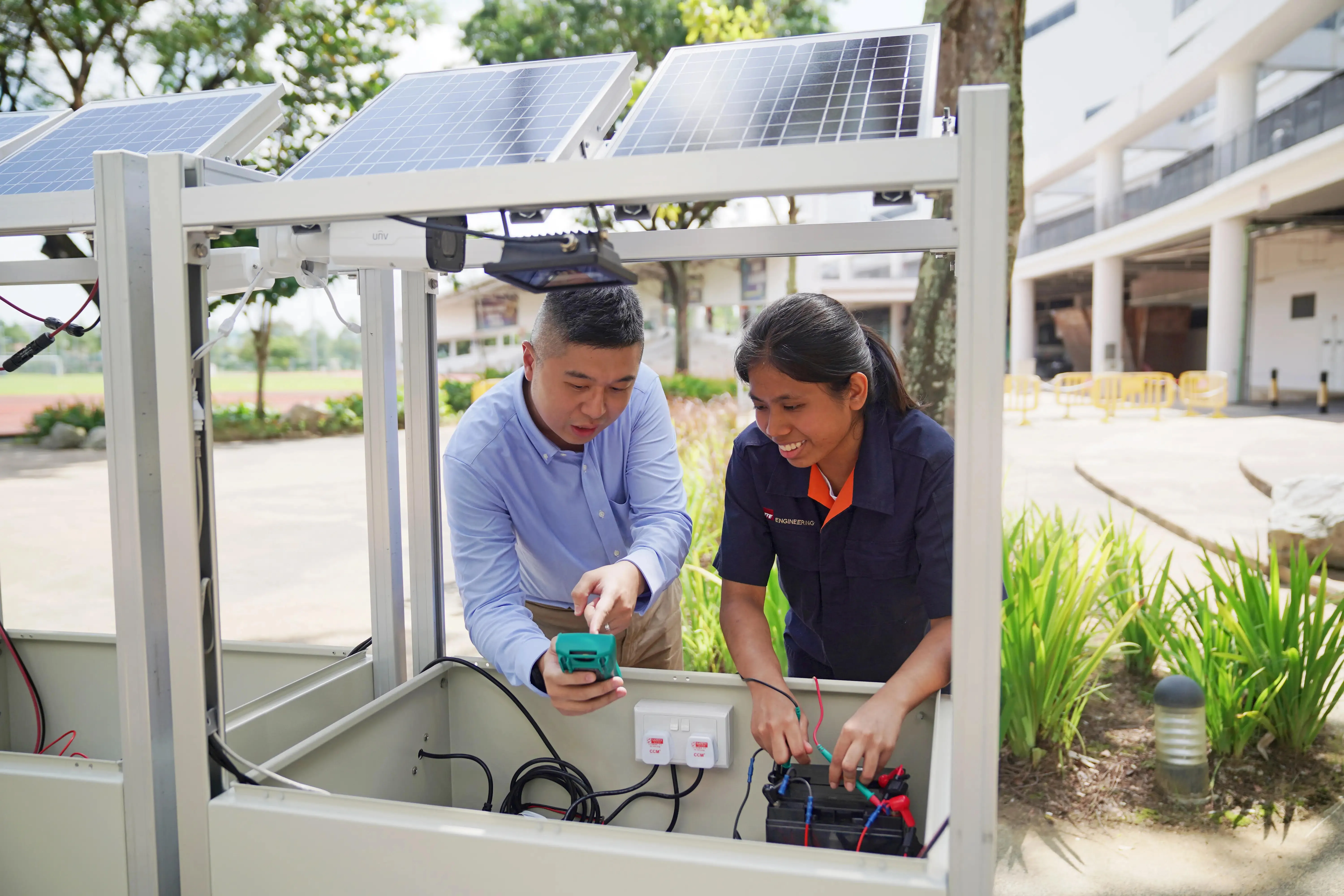 Two people work on wiring within a solar panel setup outdoors.