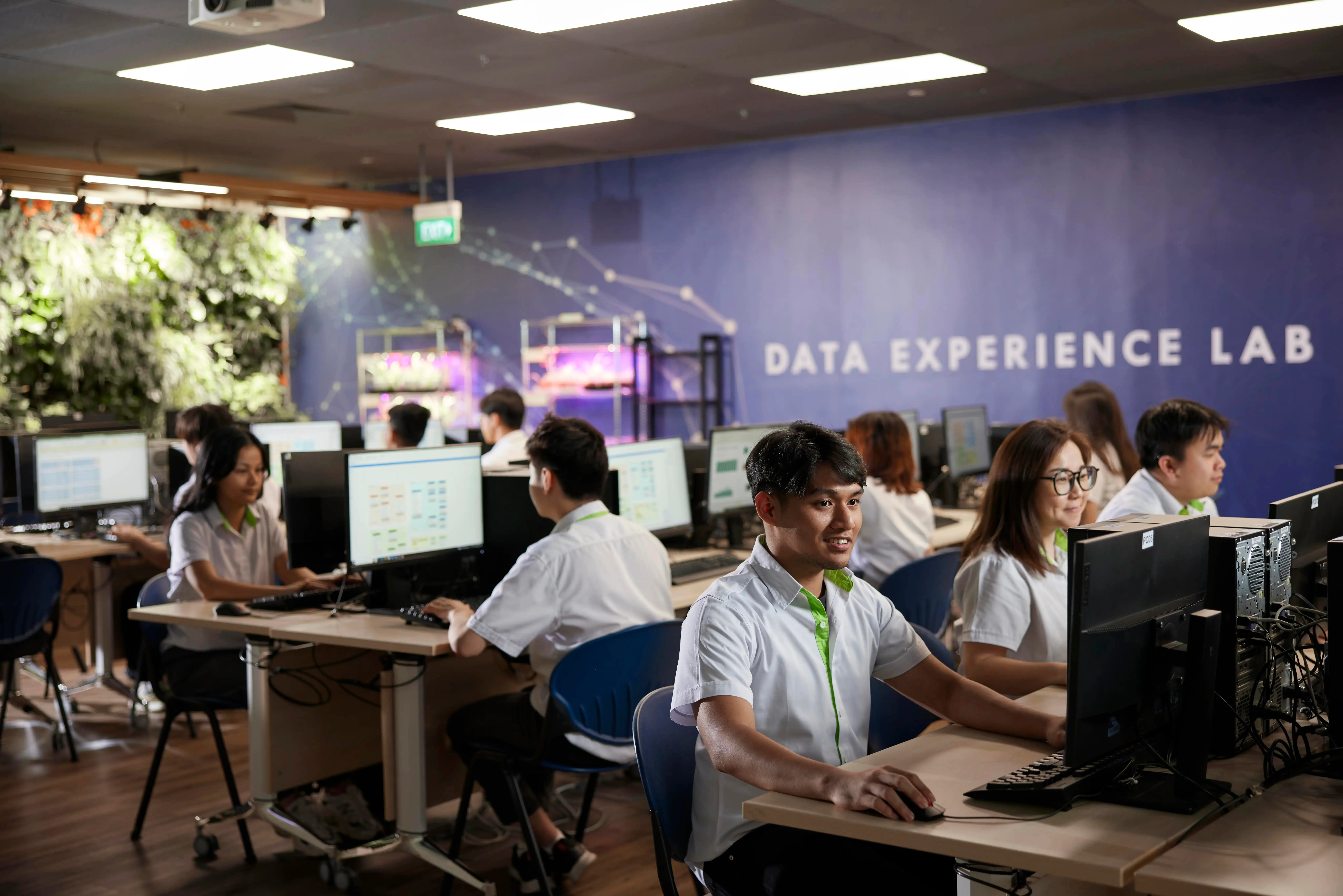 Students using computers in the /'Data Experience Lab/' wearing uniforms with green trim.