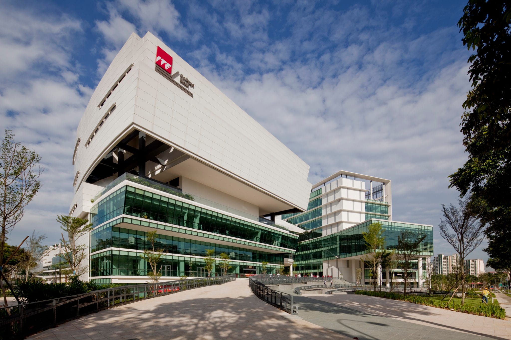 Modern ITE building with glass and white walls, under a blue sky with clouds.