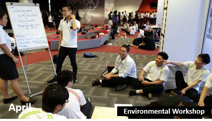 Students in a workshop sit around a whiteboard in a large hall.