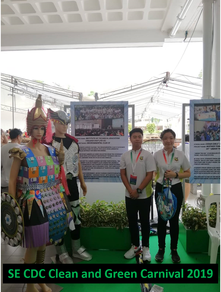 Two students stand next to mannequins dressed in upcycled materials at 'SE CDC Clean and Green Carnival 2019'.