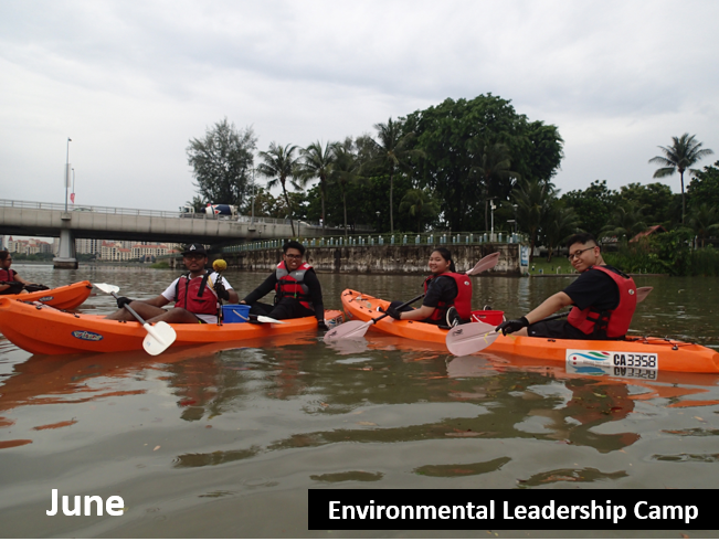 Several people in orange kayaks, wearing red life vests and holding paddles on a river.