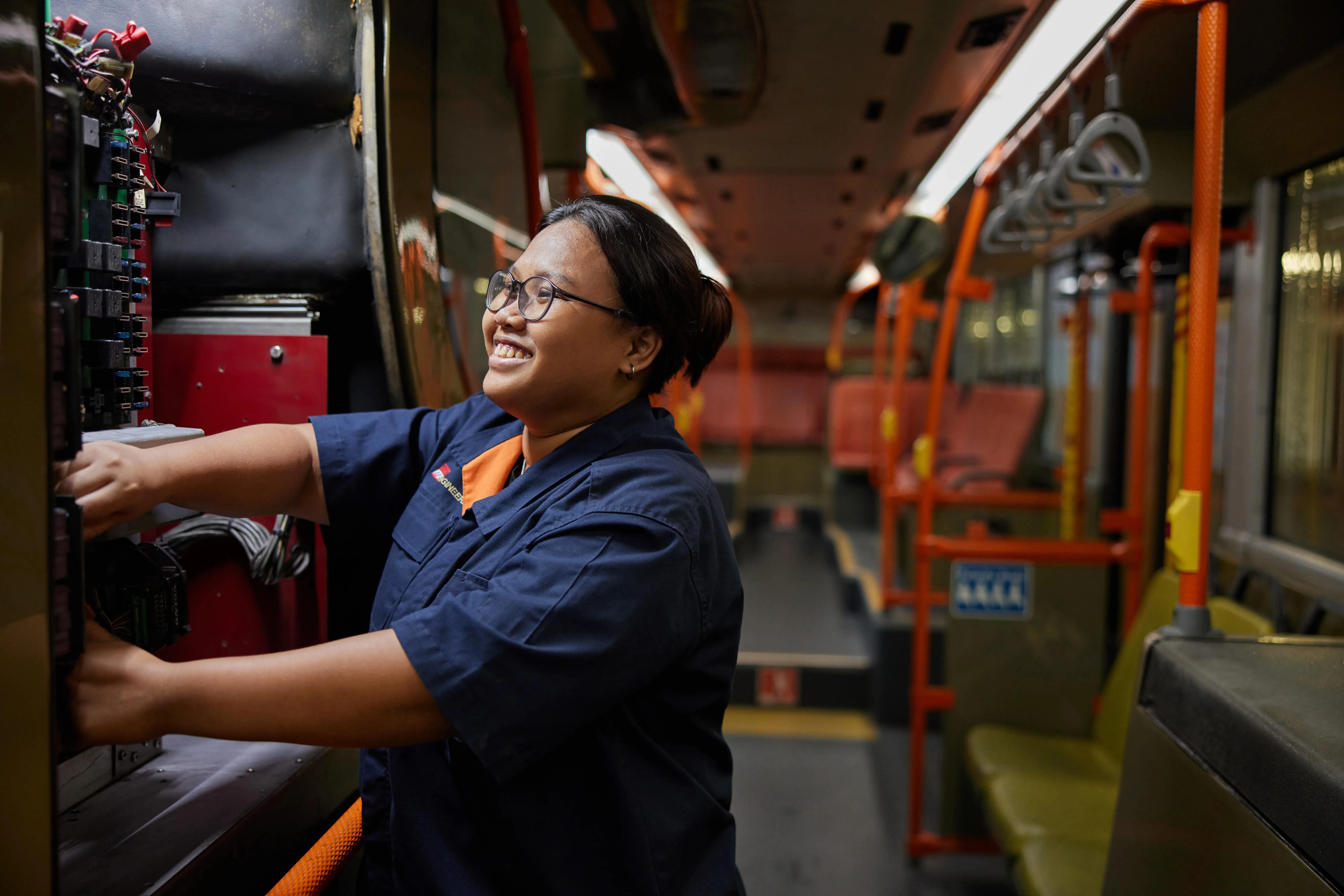 Person in workwear repairs bus control panel, interior view.