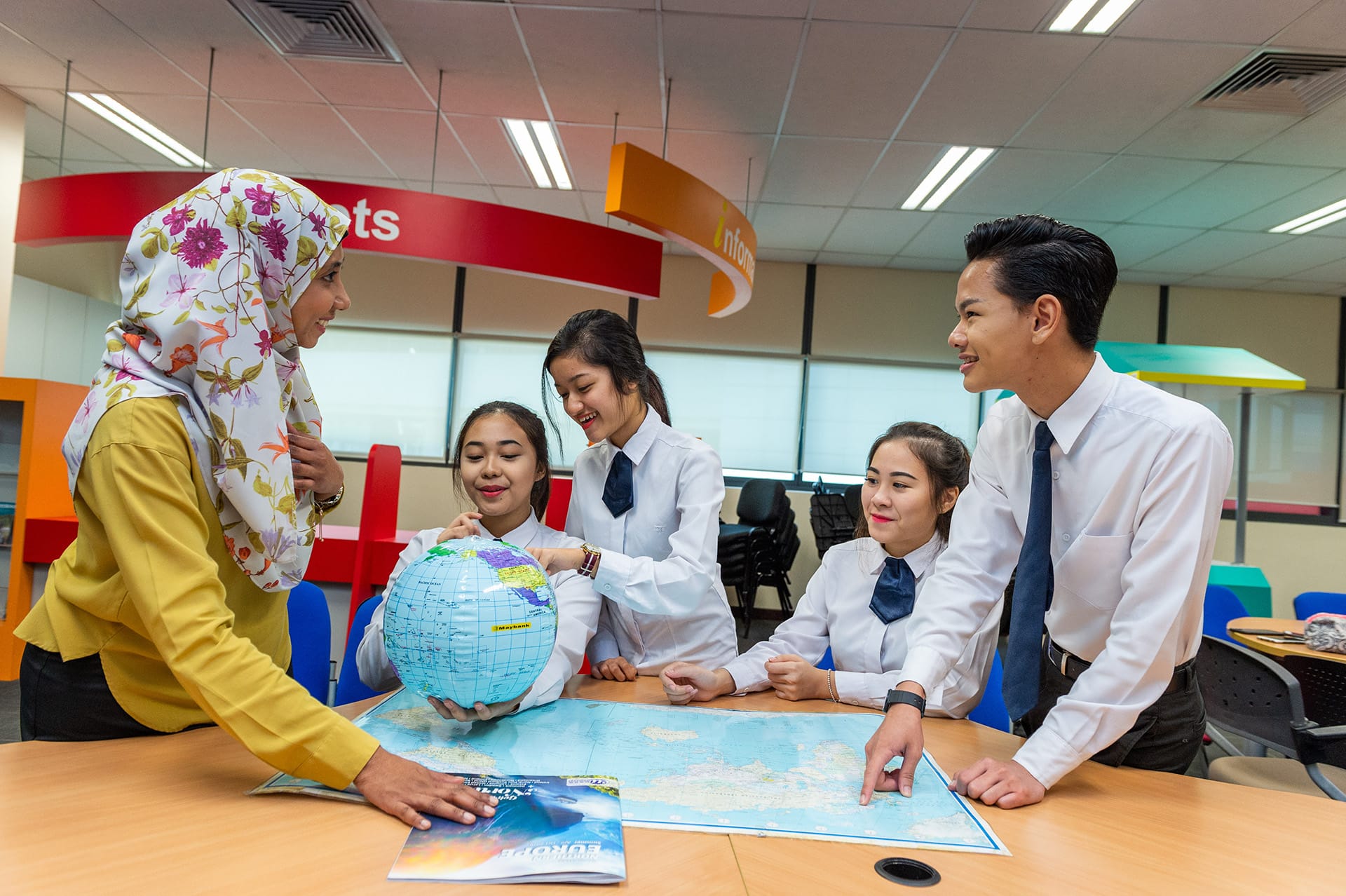 Students in uniform discussing with teacher using a globe and map in a travel classroom
