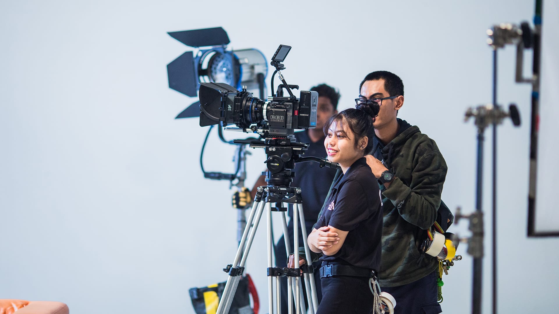 Film crew with RED camera and lights, white backdrop.