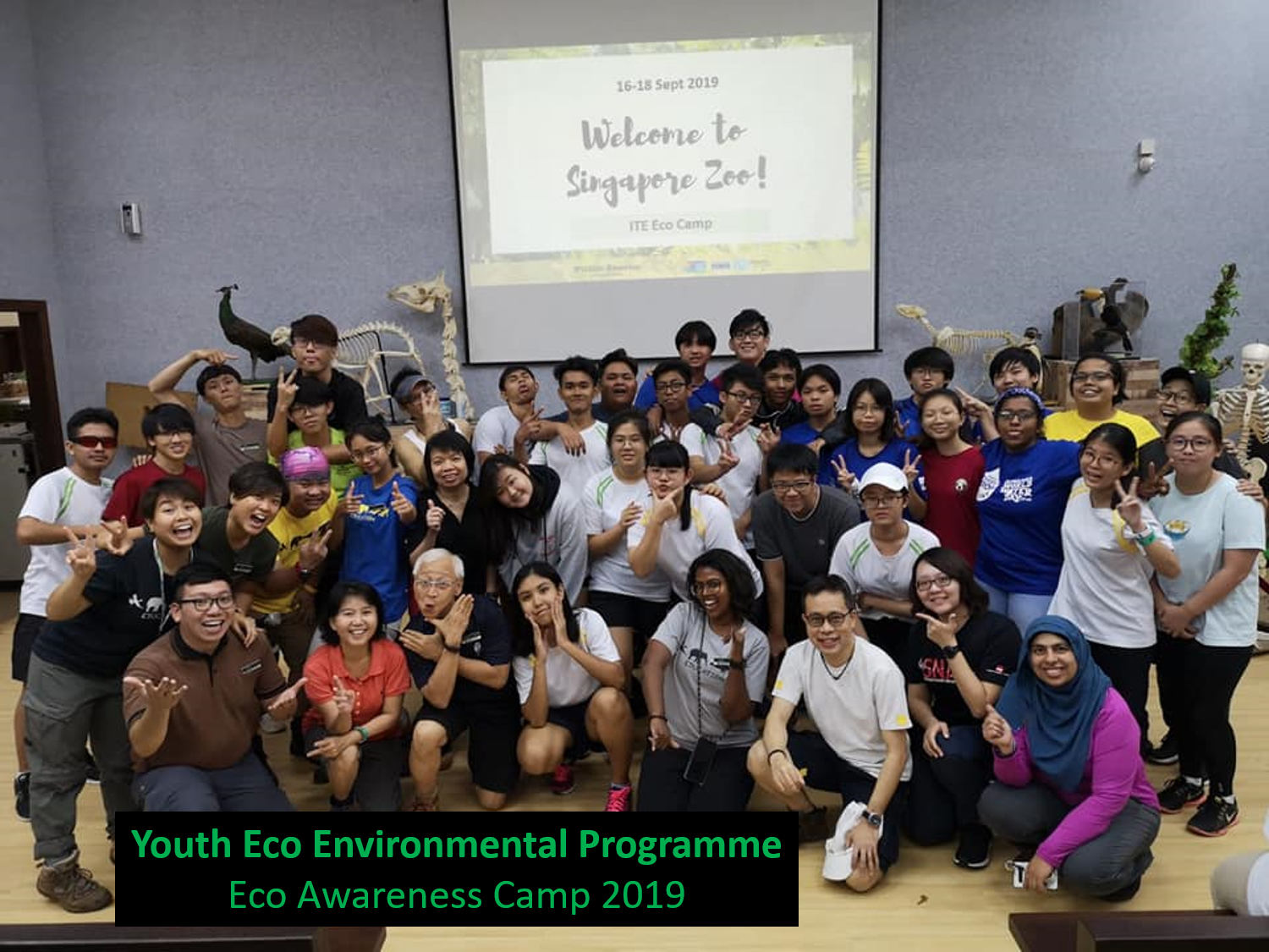 Group photo of youth at 'Welcome to Singapore Zoo!' Eco Camp with animal skeletons and peacock decor.