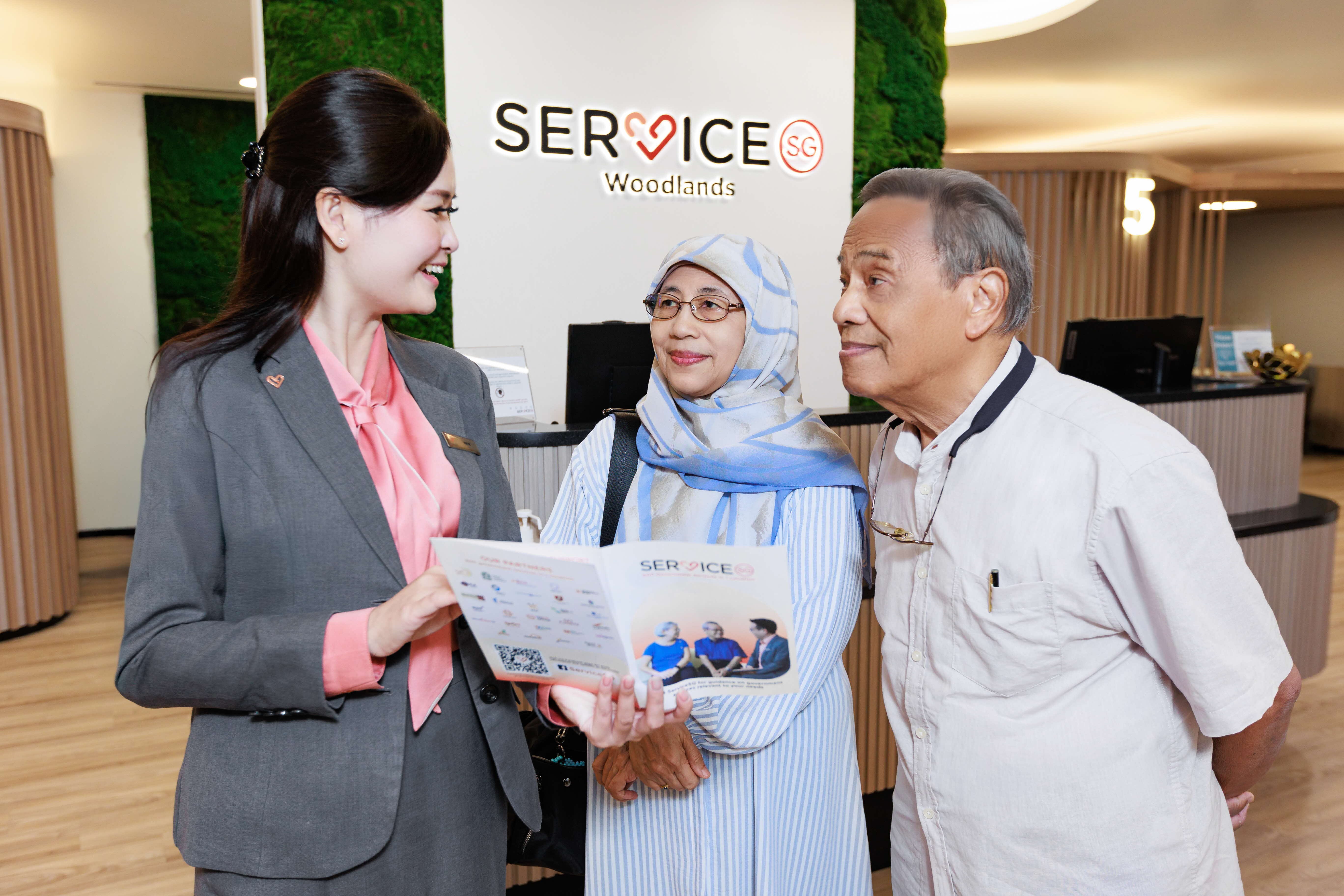 Two ServiceSG officers at the One Punggol Centre front desk with logo in background
