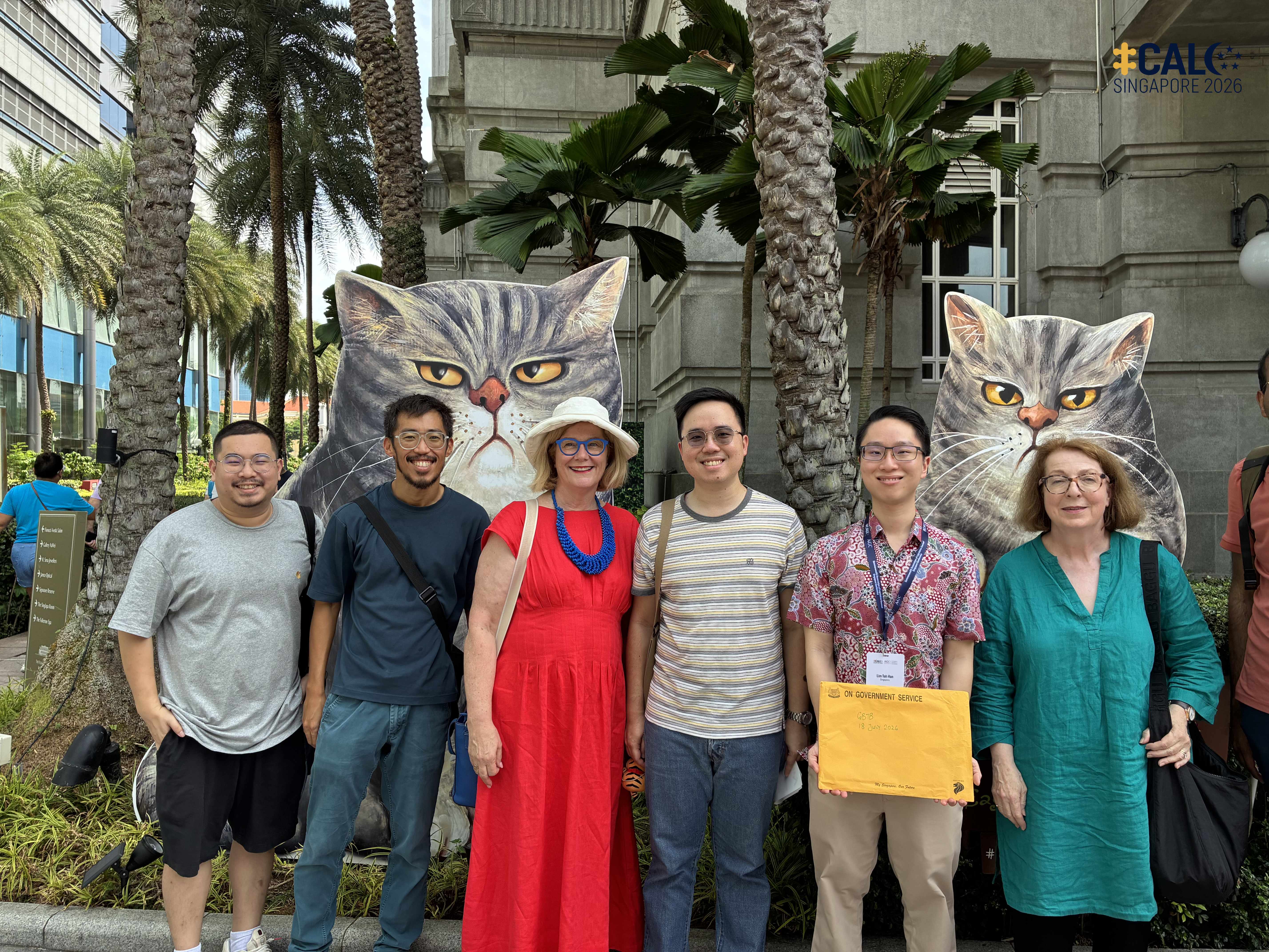 Conference delegates pose for a group photo in front of giant grumpy cat cutouts outside The Fullerton Hotel Singapore, on 18 July 2026.