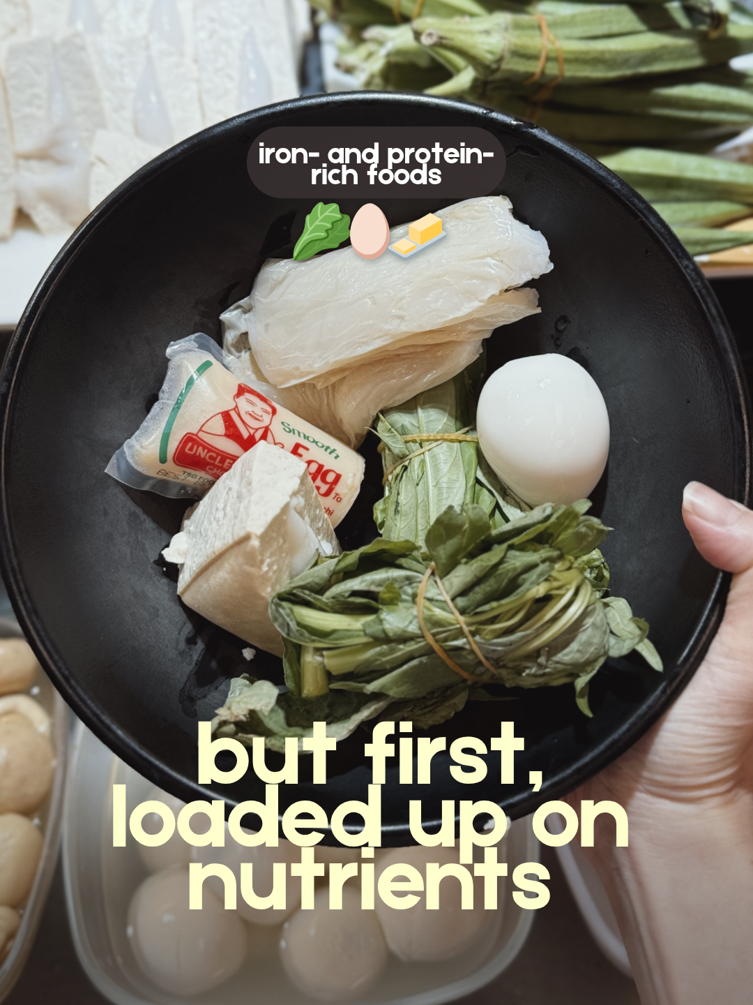 A hand holds a black bowl filled with iron- and protein-rich foods, including a boiled egg, tofu, and leafy green vegetables. The text overlay reads, "but first, loaded up on nutrients."